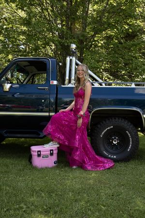A bright pink magenta lace dress contrasts against a black pickup truck and green grass in an outdoor setting.
