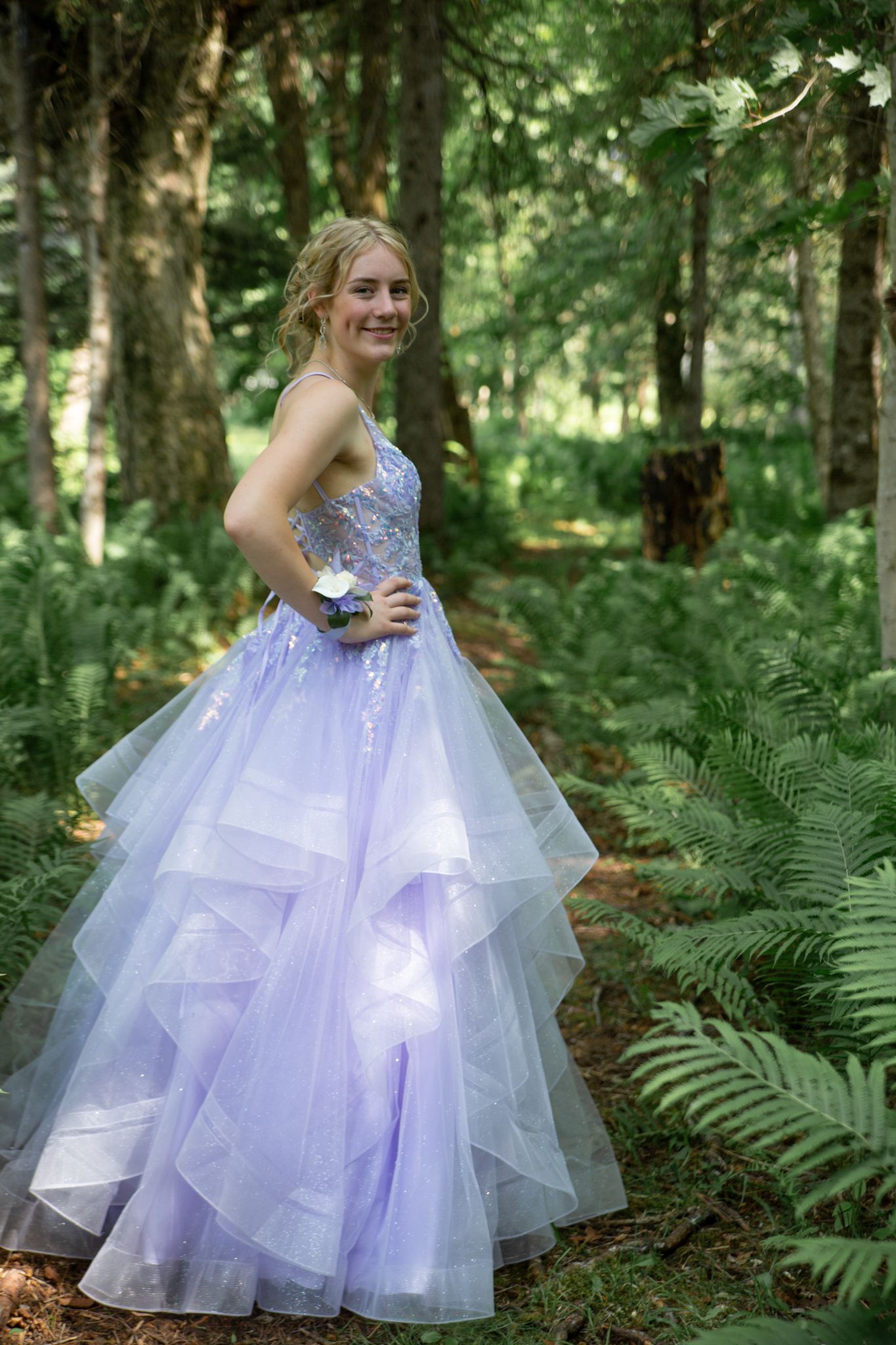 A formal lavender ball gown with sparkly embellishments and layered tulle skirt photographed in a lush forest setting.