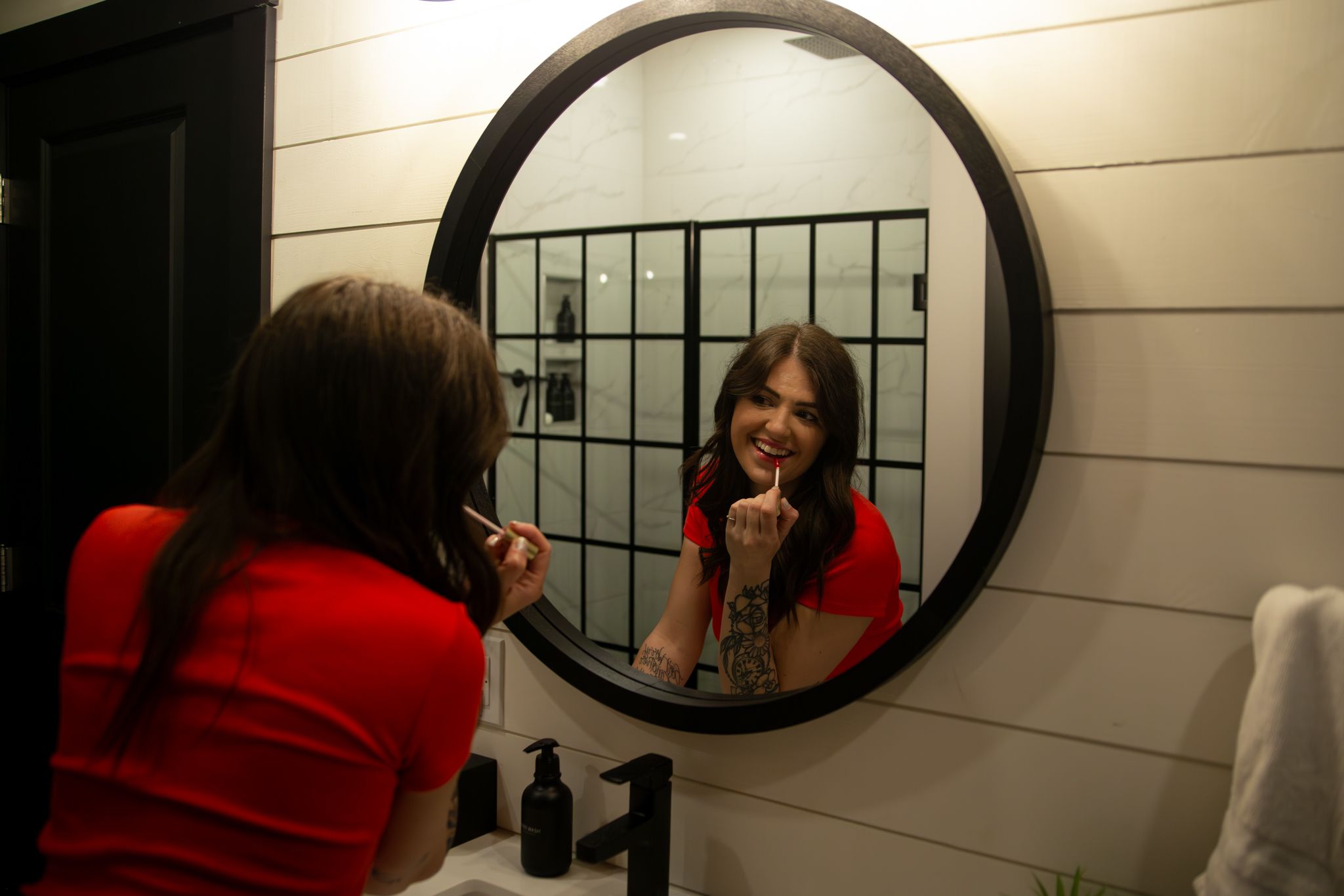 A series of mirror reflections show a person in a red sweater looking into a round mirror mounted on a white wall.