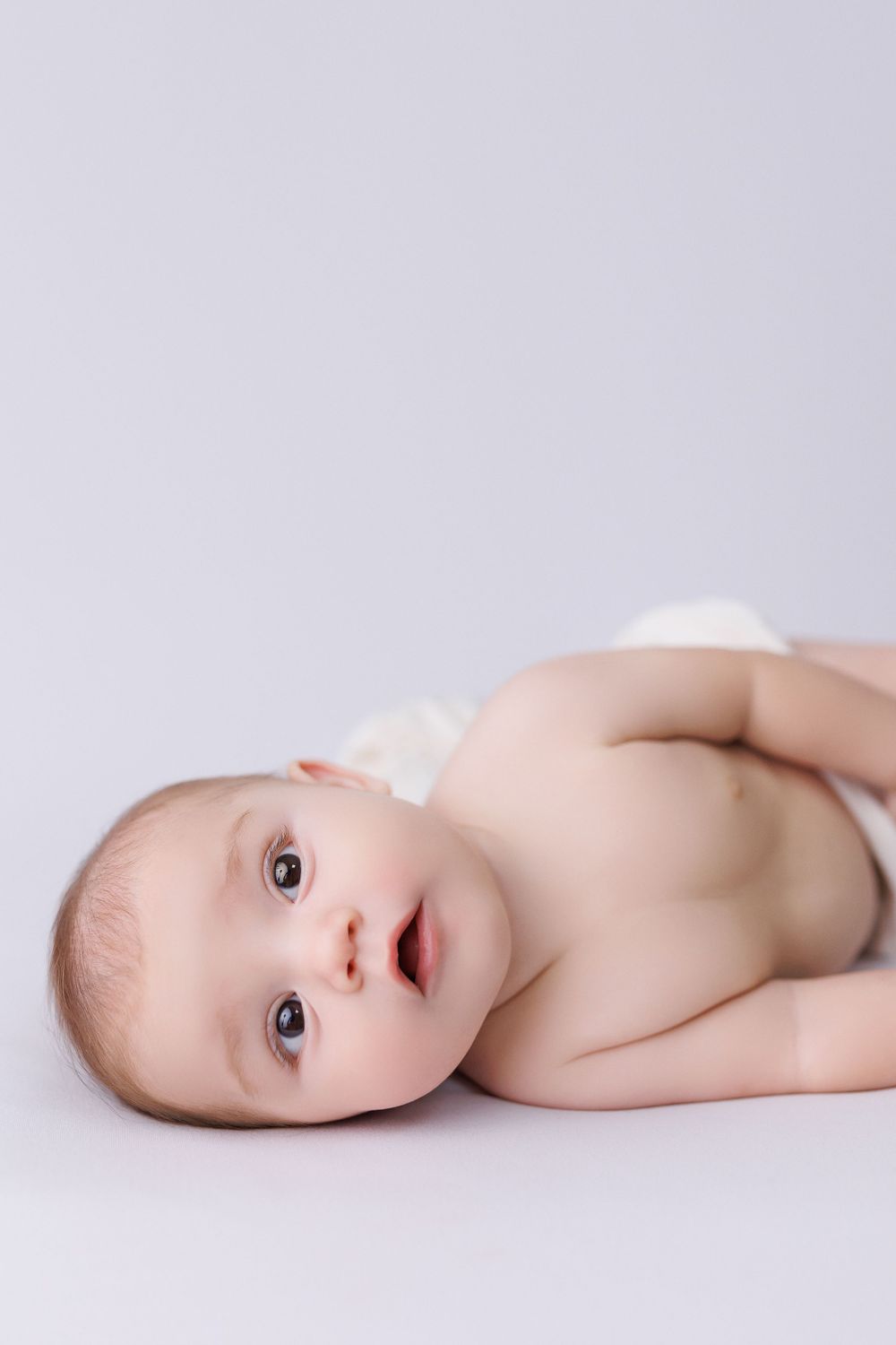 Side view of an infant lying on white backdrop during professional photoshoot.