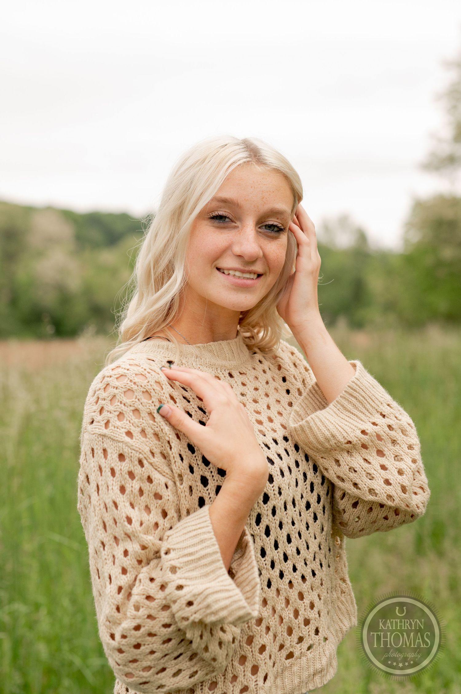 Close-up outdoor fashion portrait with beige open-knit sweater in natural meadow setting.