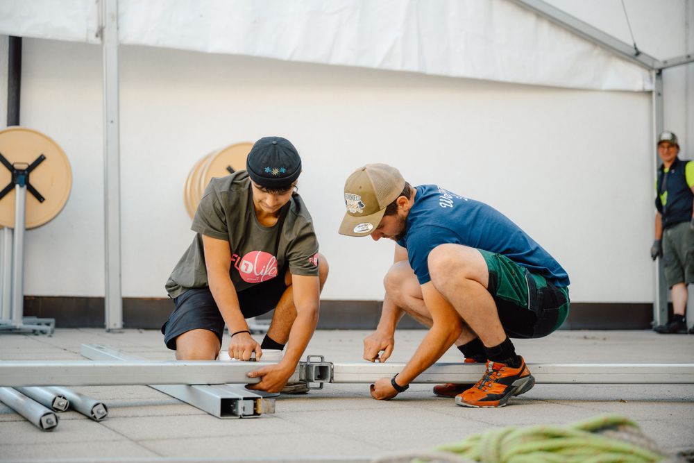Two people assembling equipment on floor in a white tent space.
