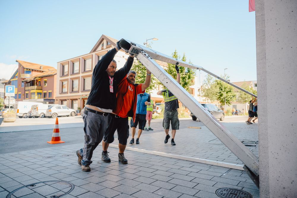 People setting up metal staging equipment outdoors near a building.