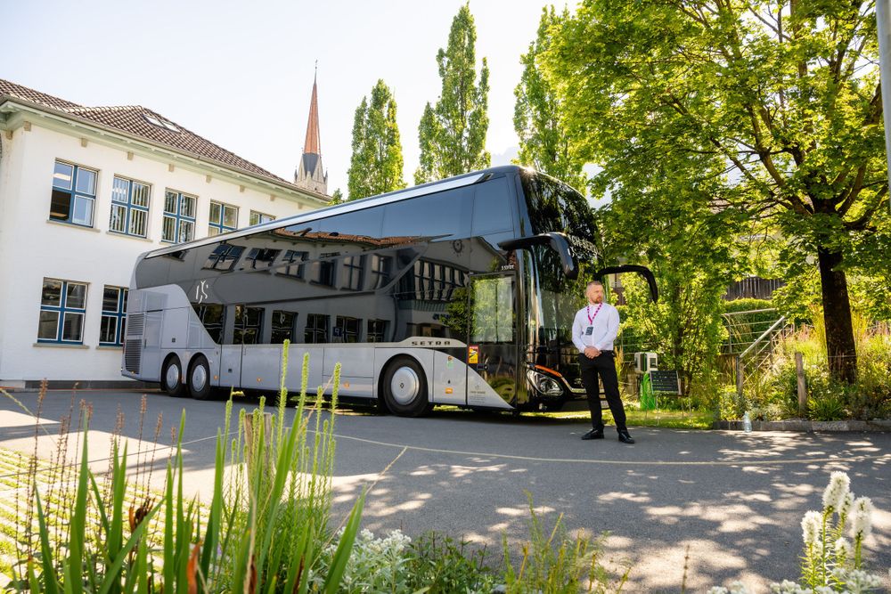 Tour bus parked outside building with trees in background.
