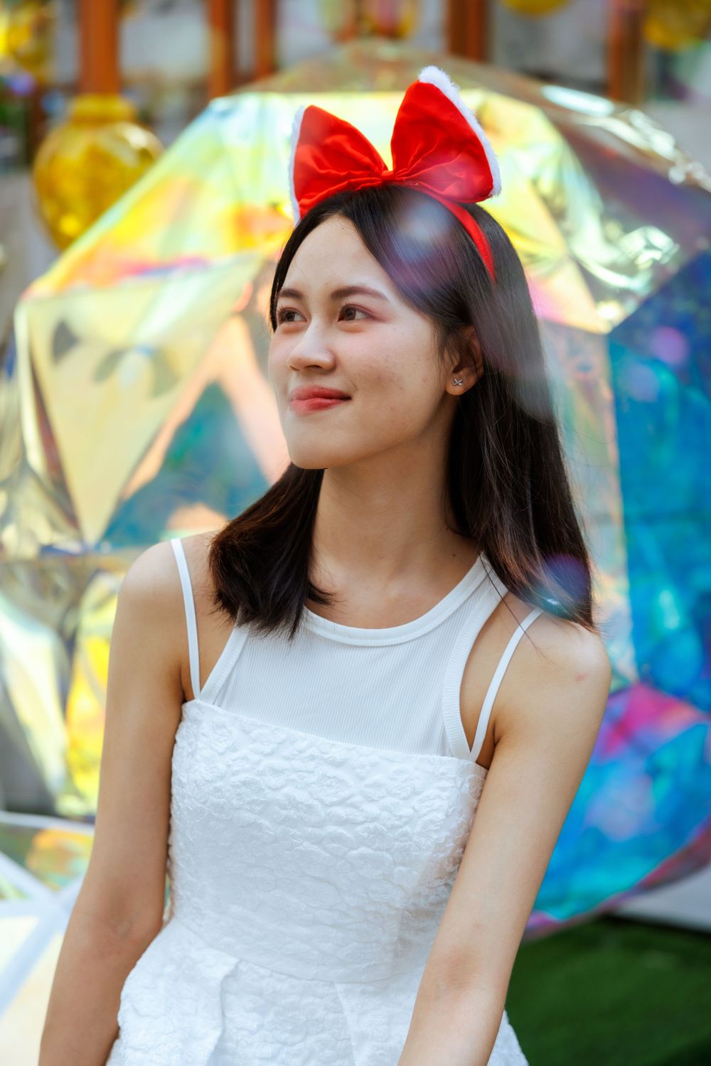 Elegant white dress and red bow shown against holographic background with festive decorations.