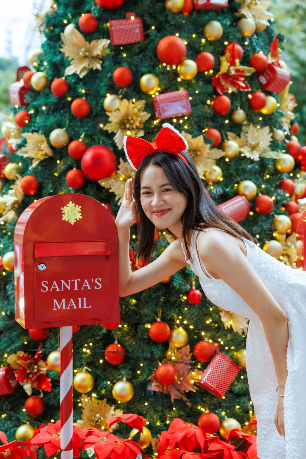 Festive pose by Santa's mailbox against decorated Christmas tree with red and gold ornaments.