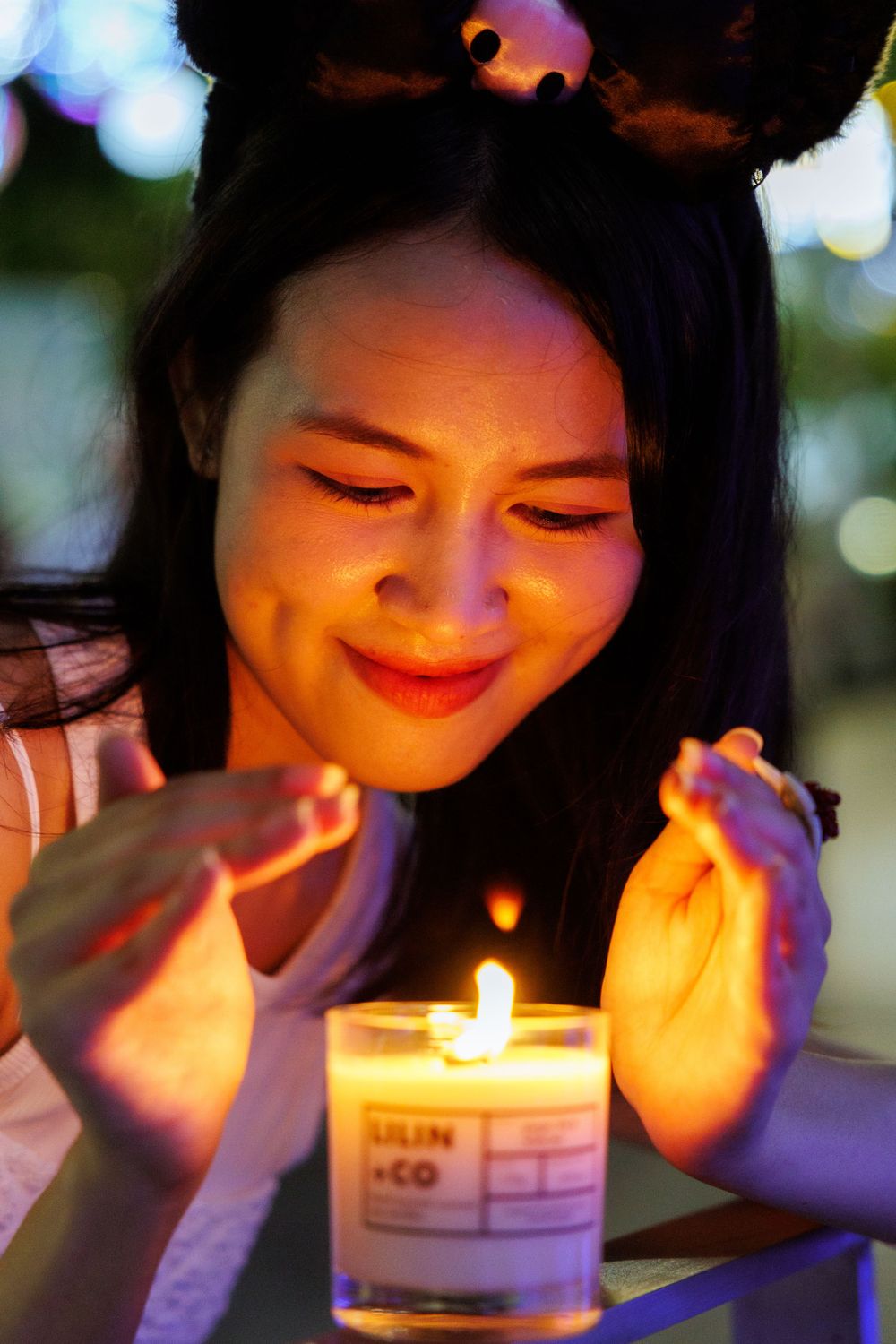 Person warming hands over lit candle with bokeh lights in background.