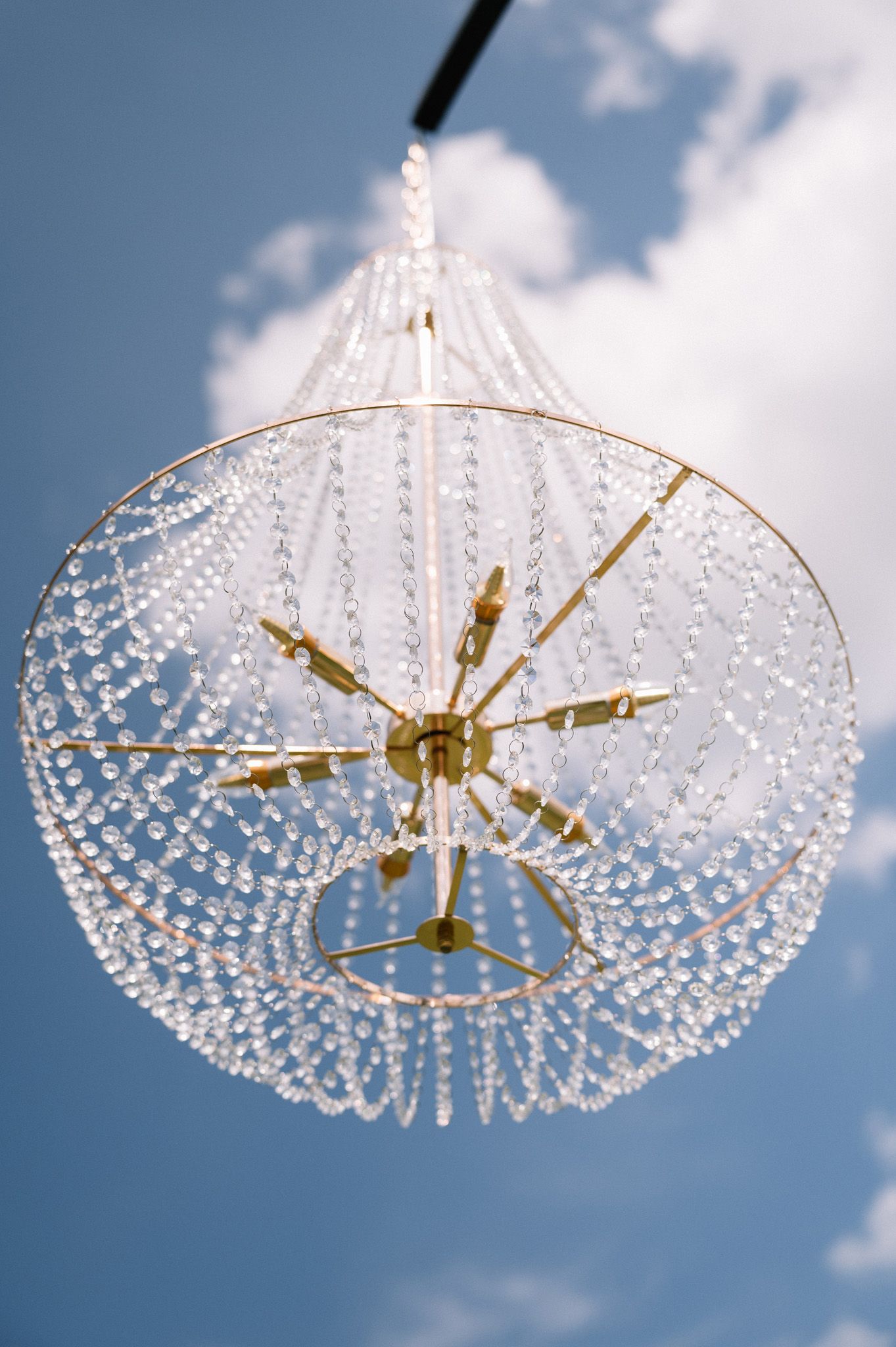 Crystal chandelier with gold accents photographed against a blue sky with white clouds.