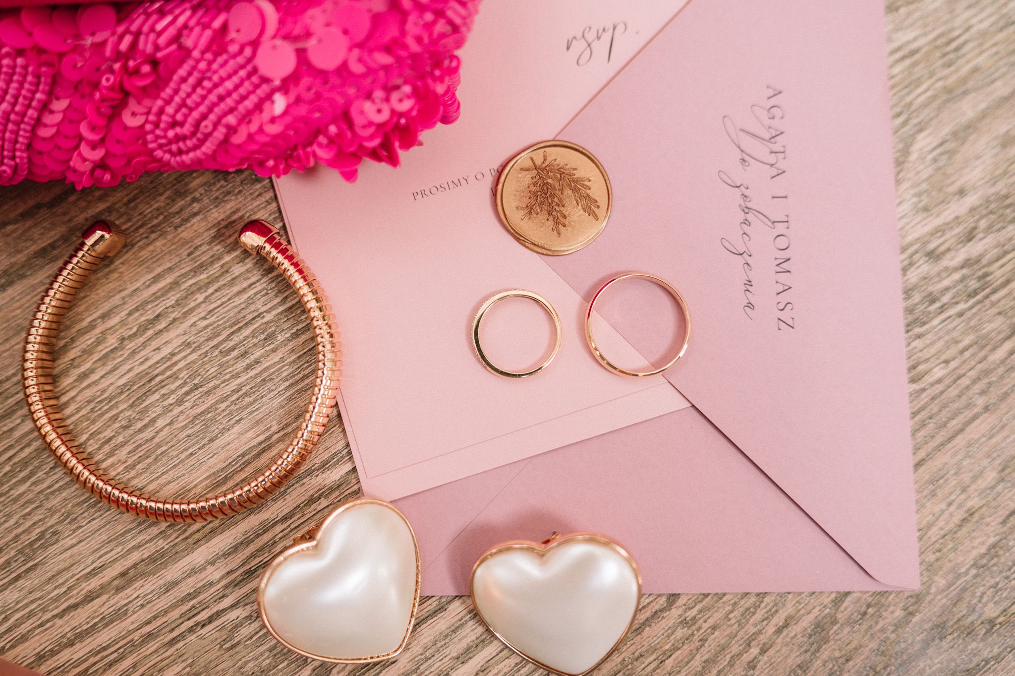 Wedding accessories including heart-shaped jewelry and pink envelopes on wooden surface.