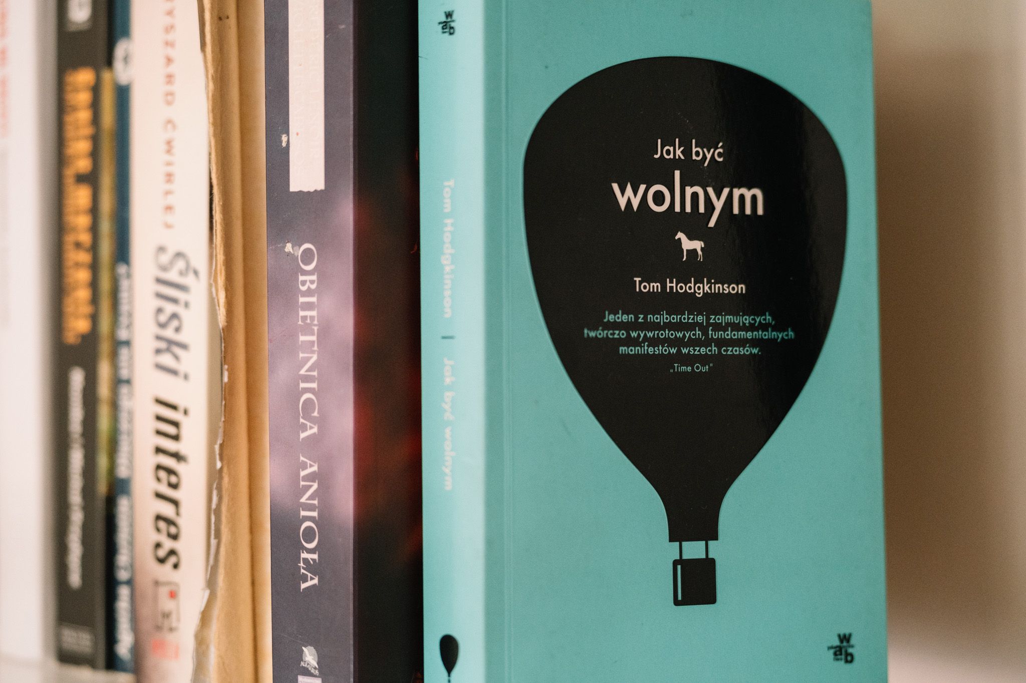 A green hardcover book with a black hot air balloon design on the spine stands between other books on a shelf.