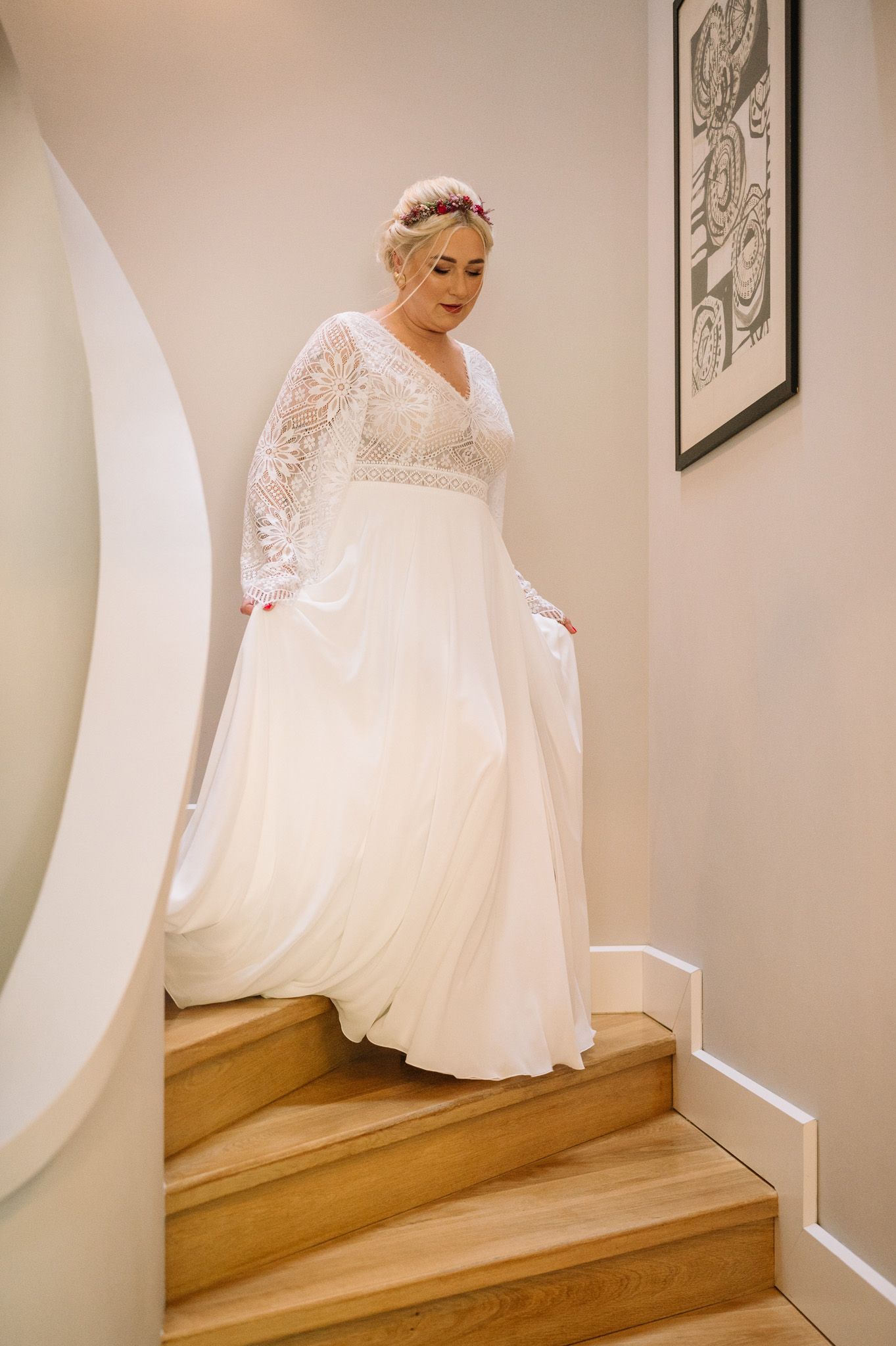 An elegant lace wedding dress on display as someone descends wooden stairs.