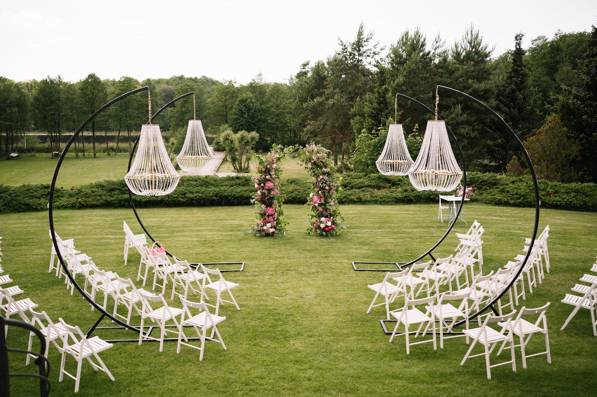 An outdoor wedding ceremony setup with hanging chairs and white folding chairs arranged in semicircles on grass.