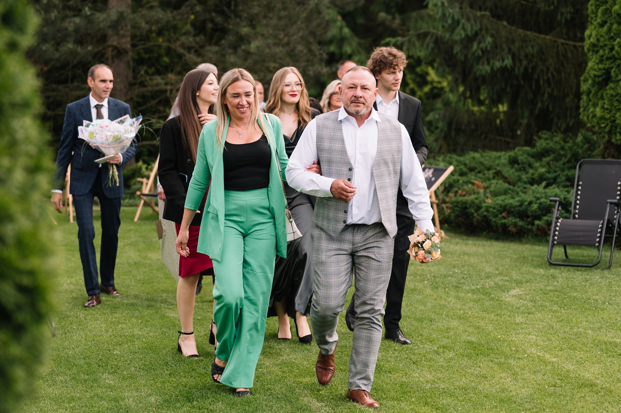 Wedding guests walk across a lush green lawn during an outdoor celebration.