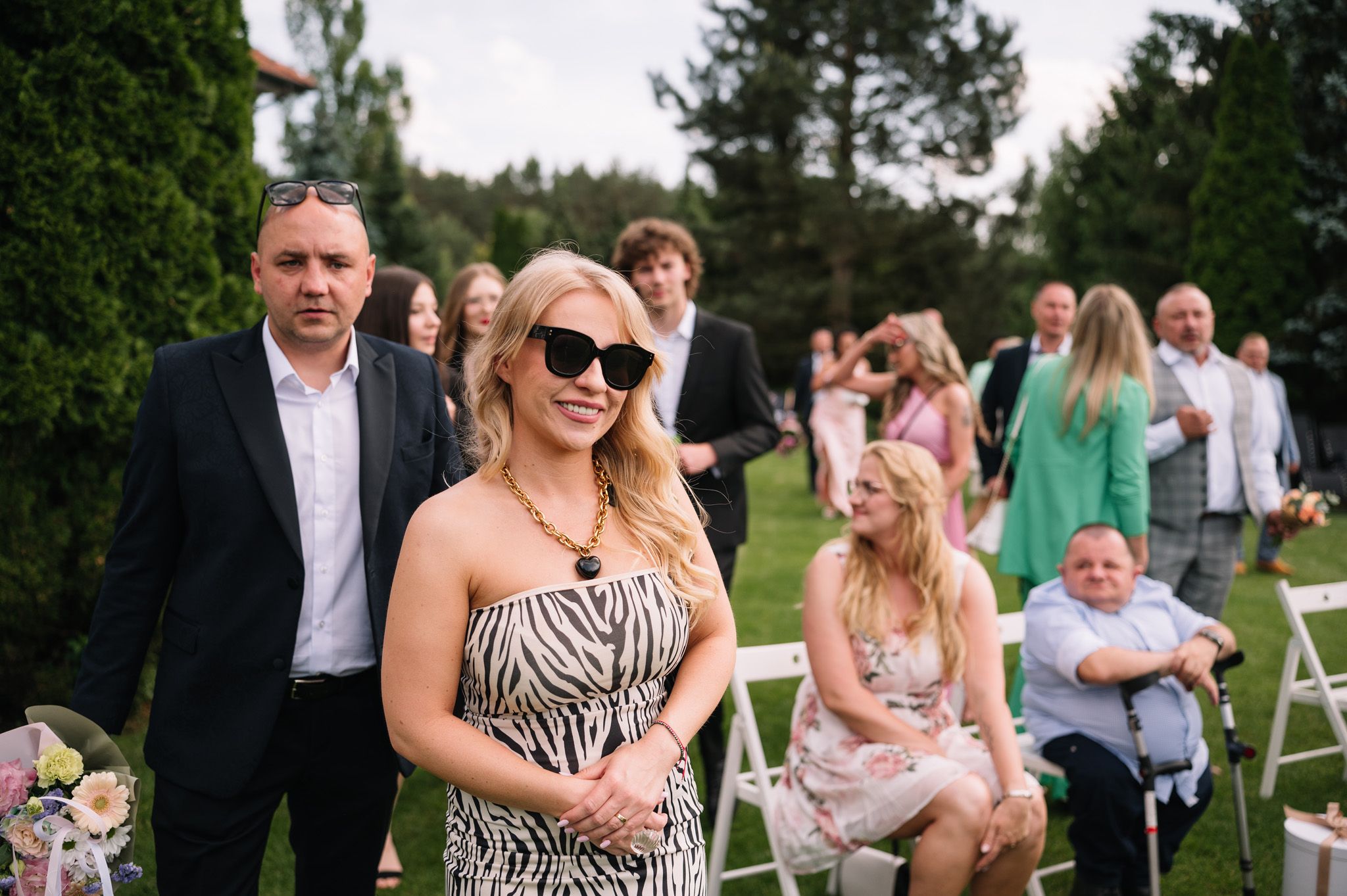 Guests in summer attire enjoy an outdoor wedding celebration with white folding chairs.