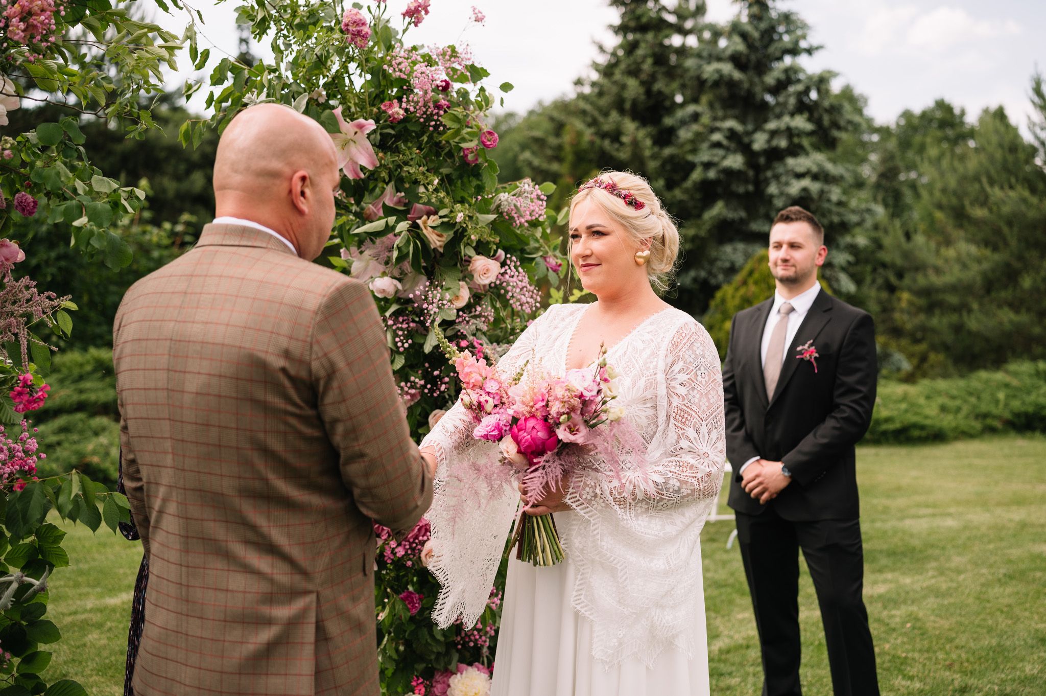 Couple exchanges vows under floral arch during outdoor garden ceremony.