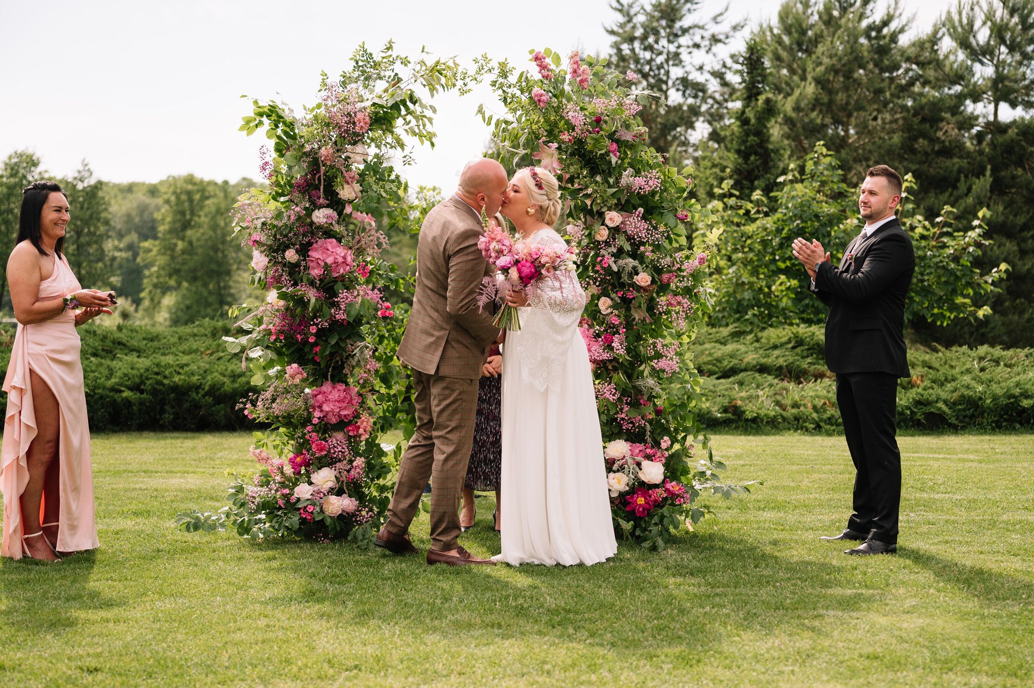 Wedding ceremony under floral arch with pink roses in garden setting.