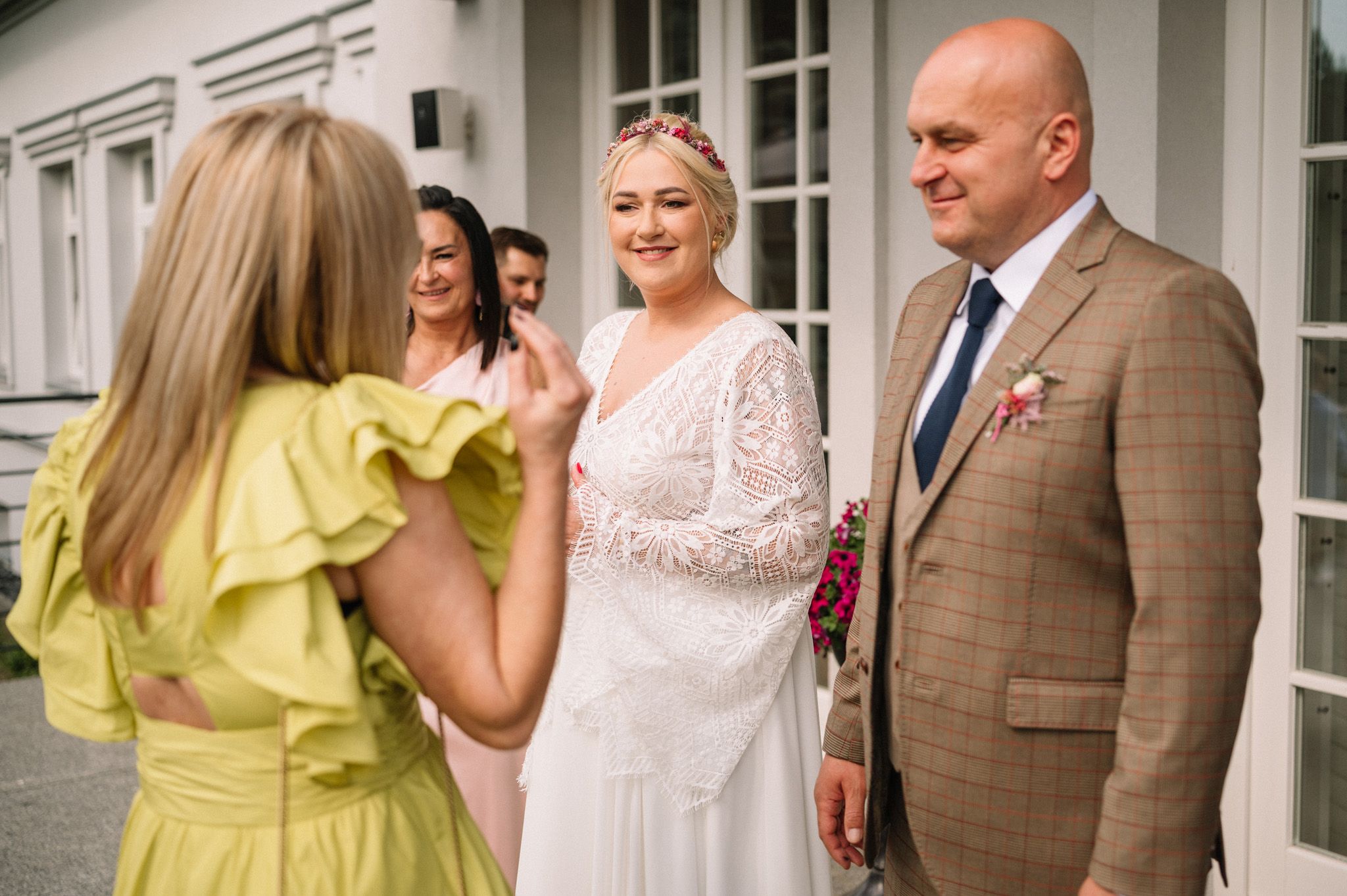 Wedding party gathered outside a white building with someone wearing a yellow dress.