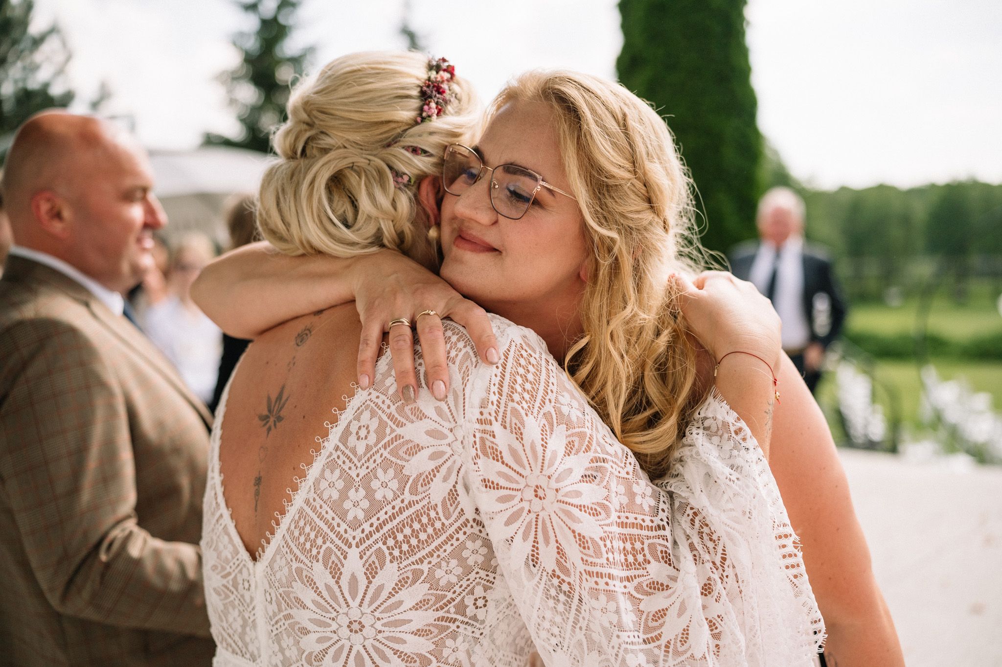 Two wedding guests share an emotional embrace while wearing elegant lace dresses.