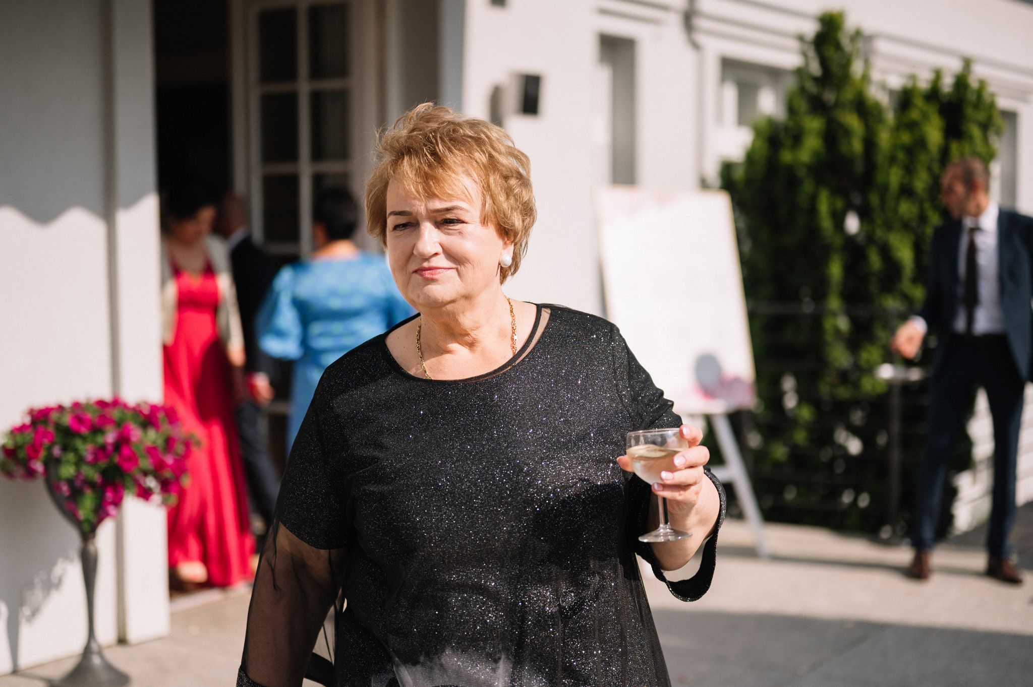 Guest enjoys a drink at an outdoor wedding reception near blooming flowers.