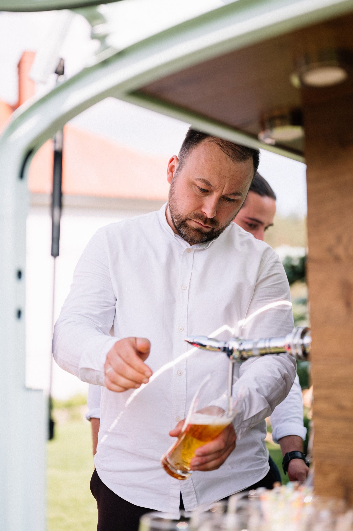 Bartender in white shirt pouring craft beer at outdoor event.