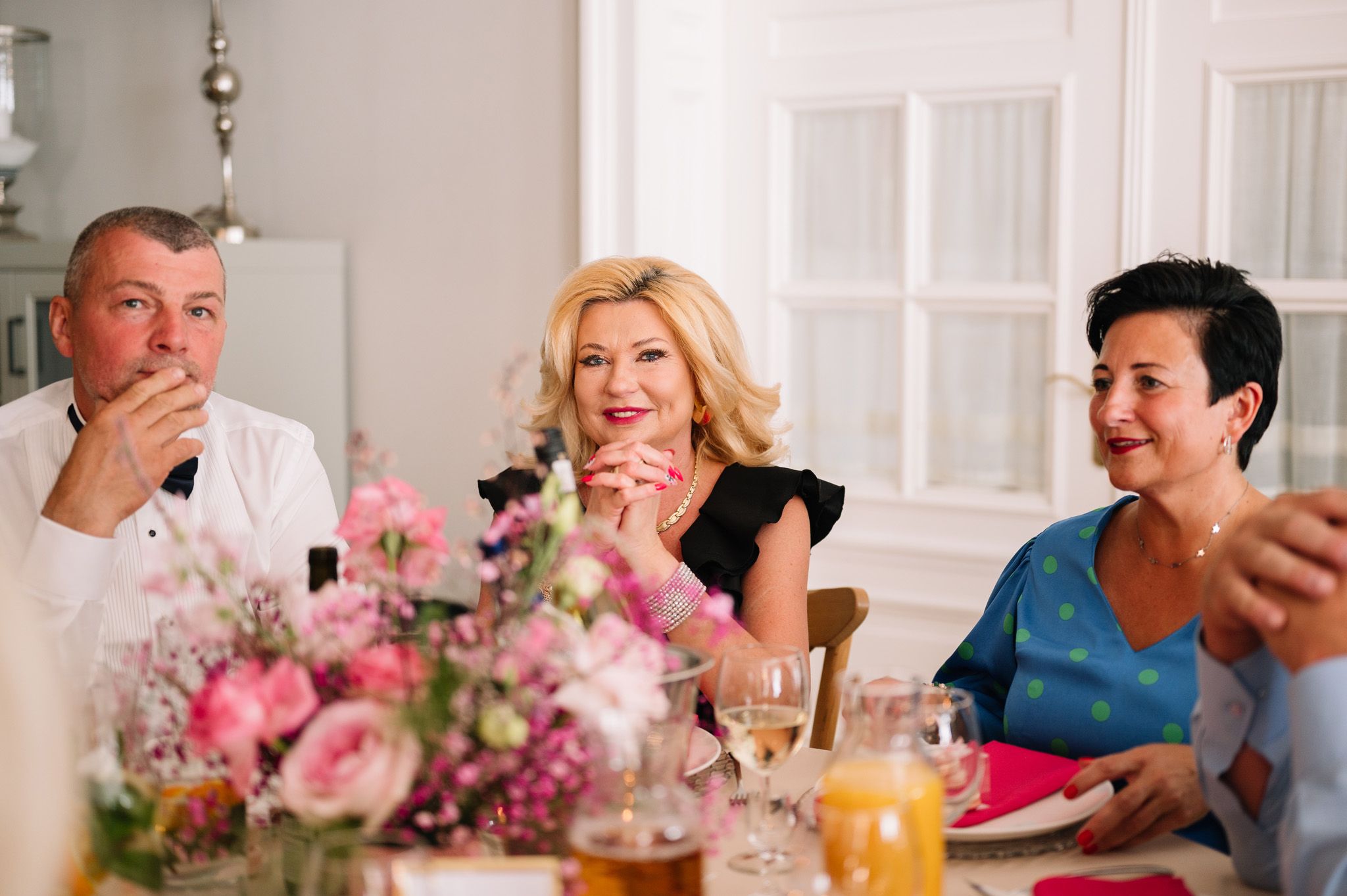 Elegant dinner party scene with beautiful pink floral centerpiece and guests enjoying conversation.