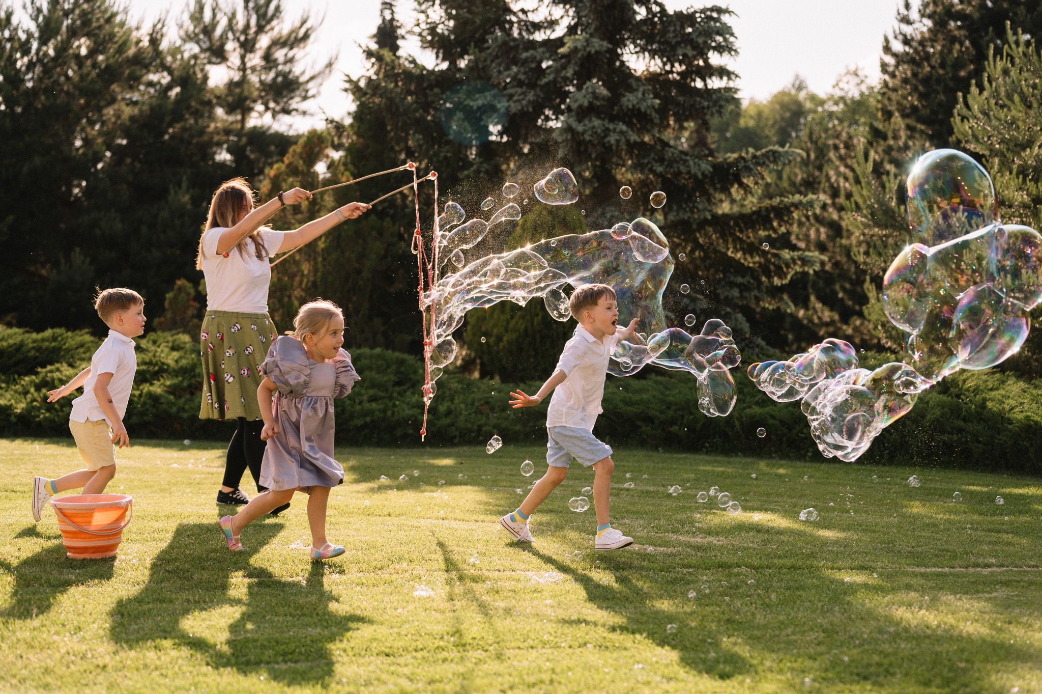 Children playing with giant bubbles on a sunny lawn during summer outdoor activities.