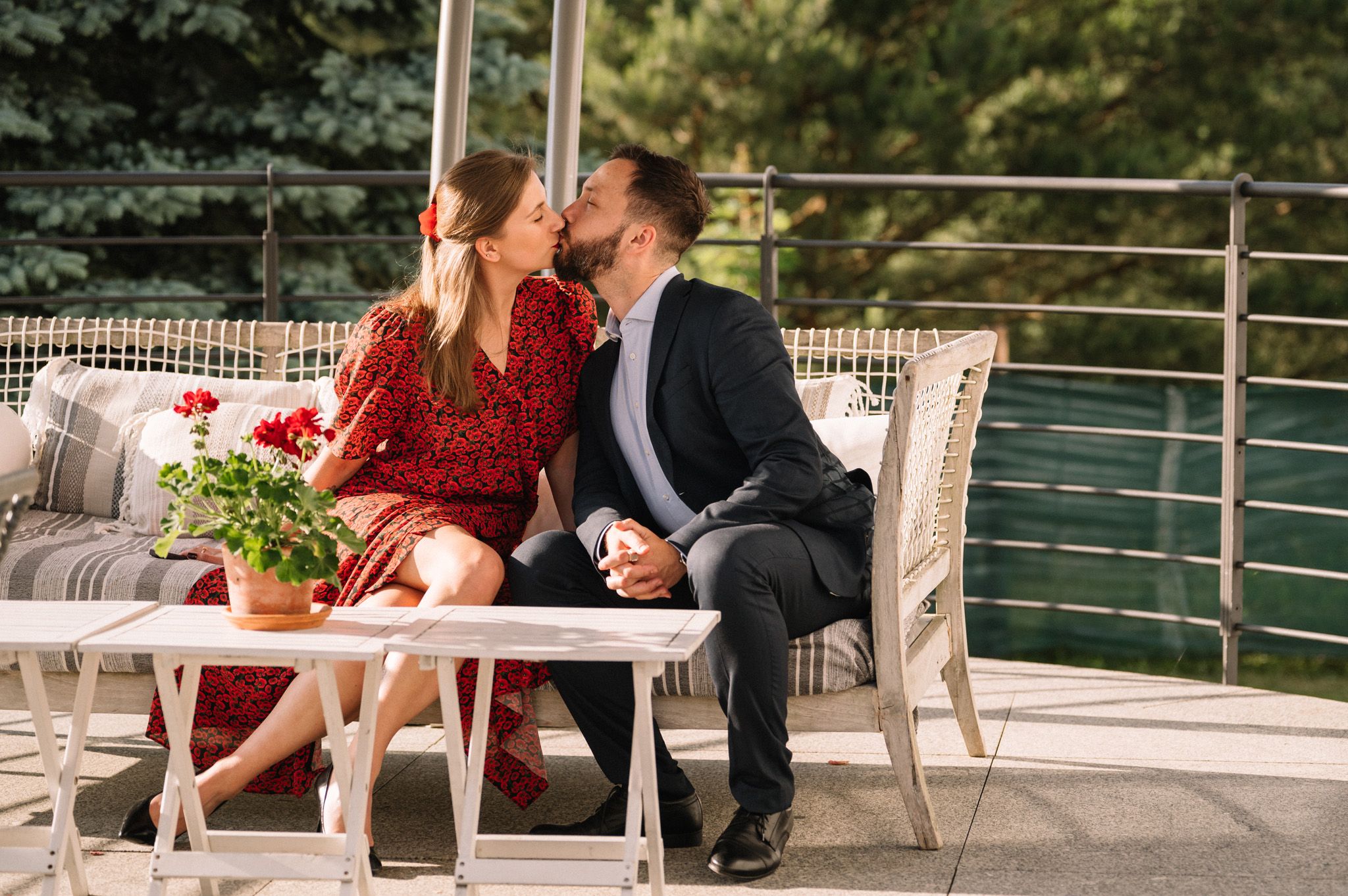 A romantic couple sharing an intimate moment on an outdoor patio with red flowers and modern furniture.
