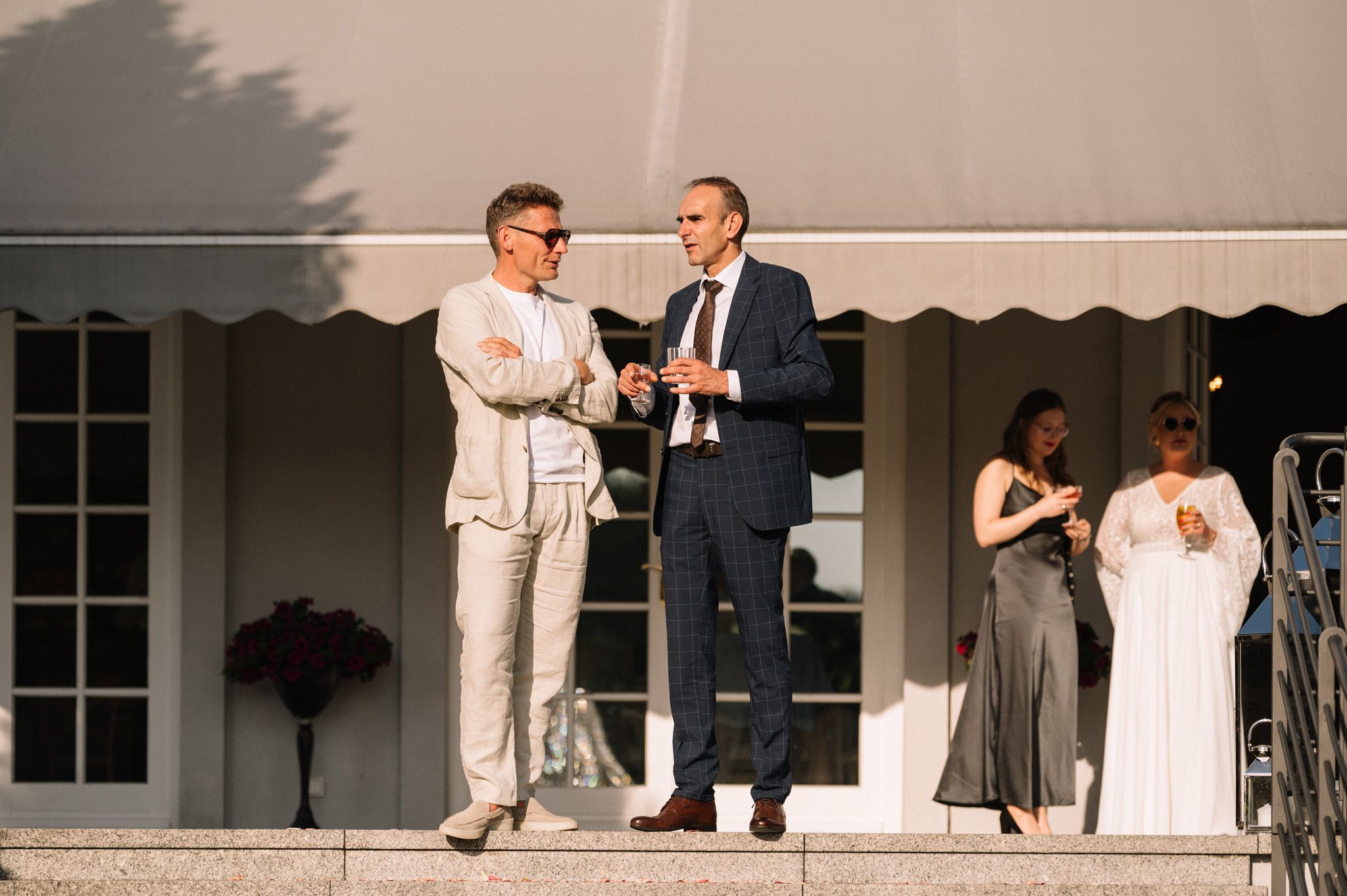 Two people in formal attire sharing drinks on a terrace during an elegant event.