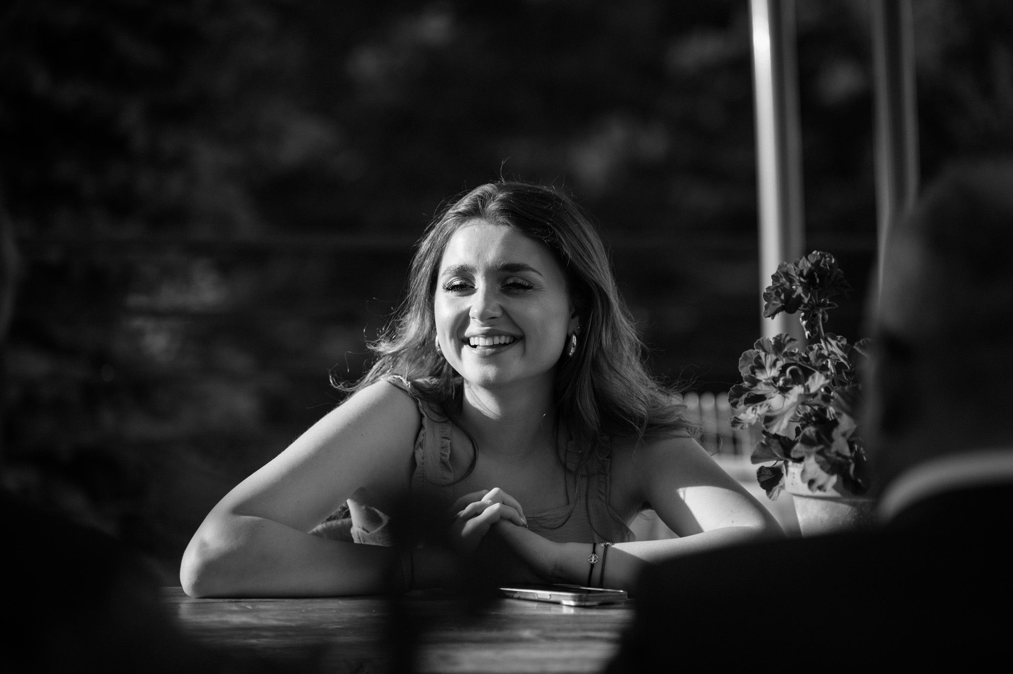 Black and white portrait of someone smiling at an outdoor table.