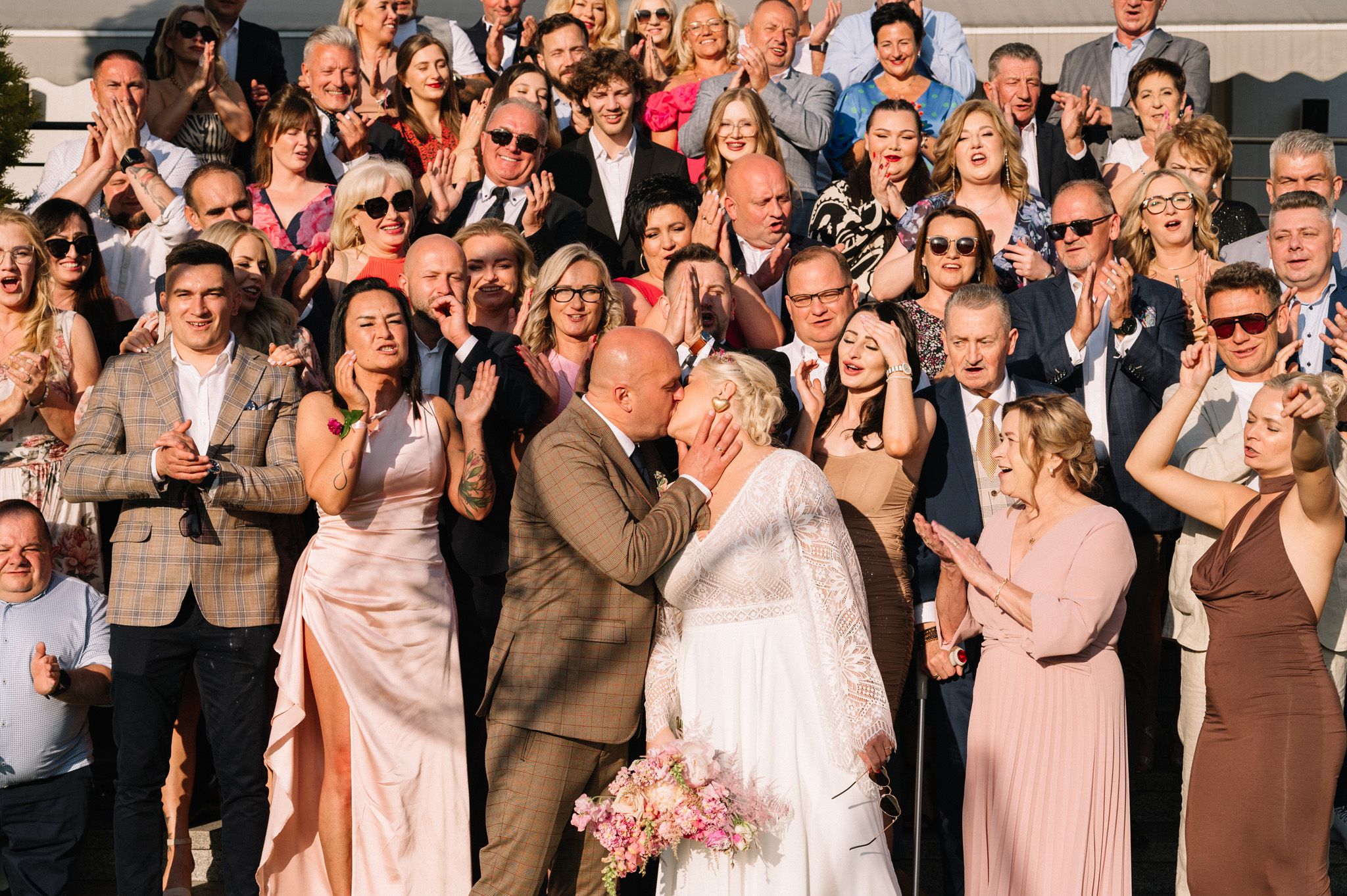 Large group of wedding guests applauding during an outdoor celebration.