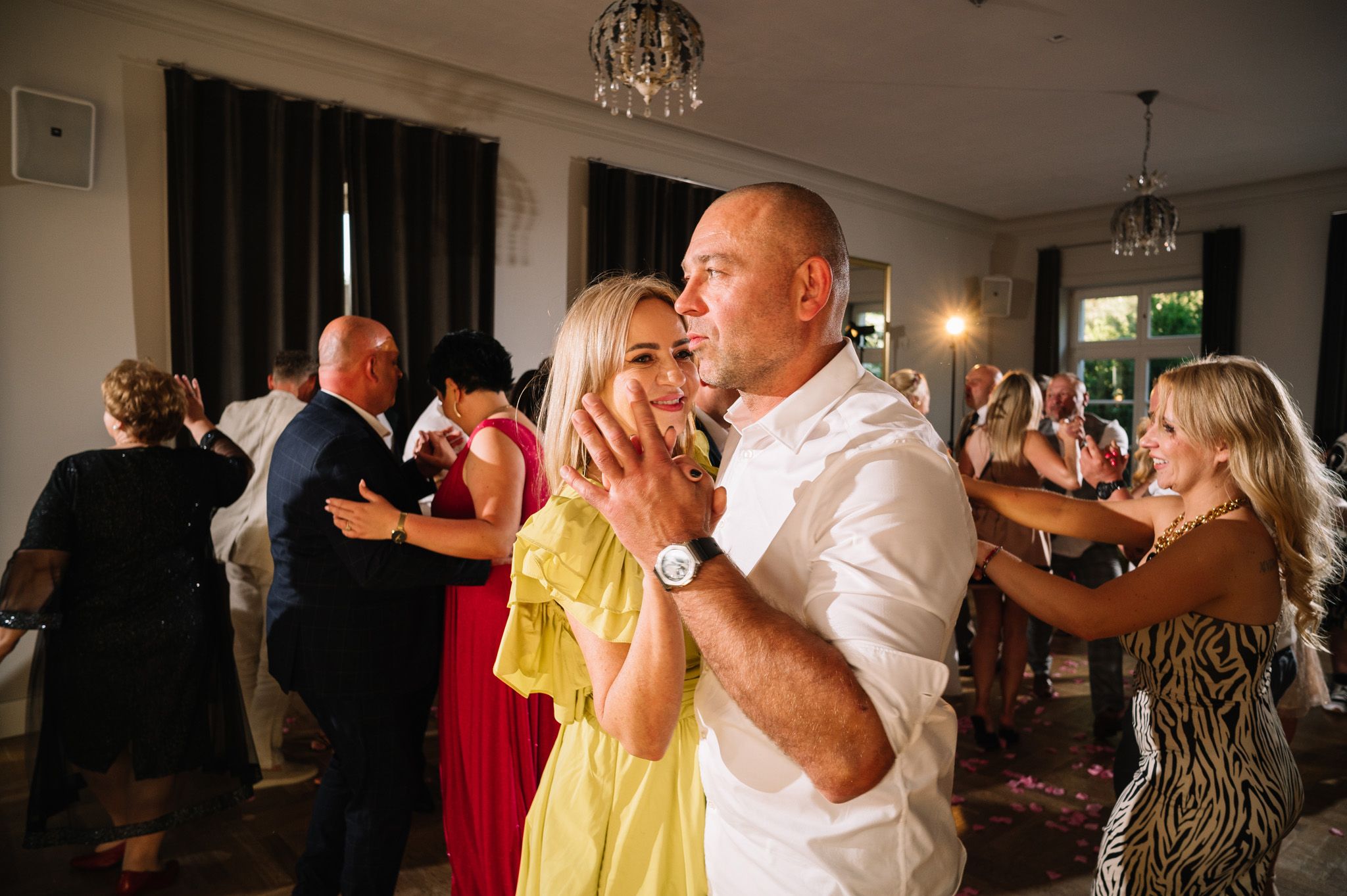 Wedding reception guests dancing and celebrating on the dance floor under chandelier lighting.