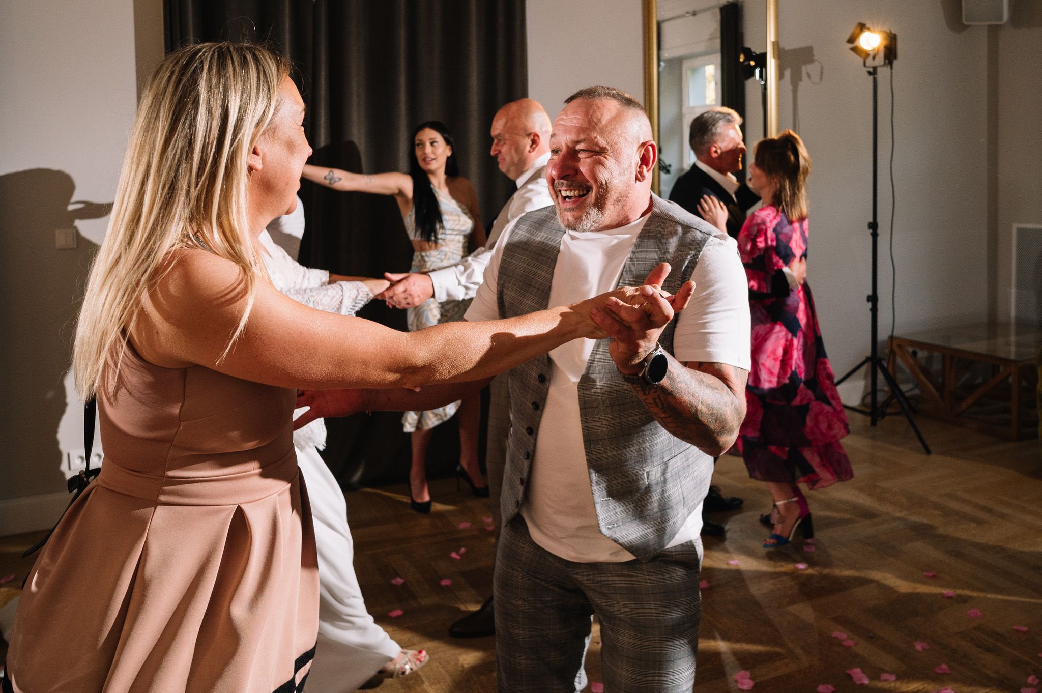 Party guests dancing energetically on wooden dance floor during wedding celebration.