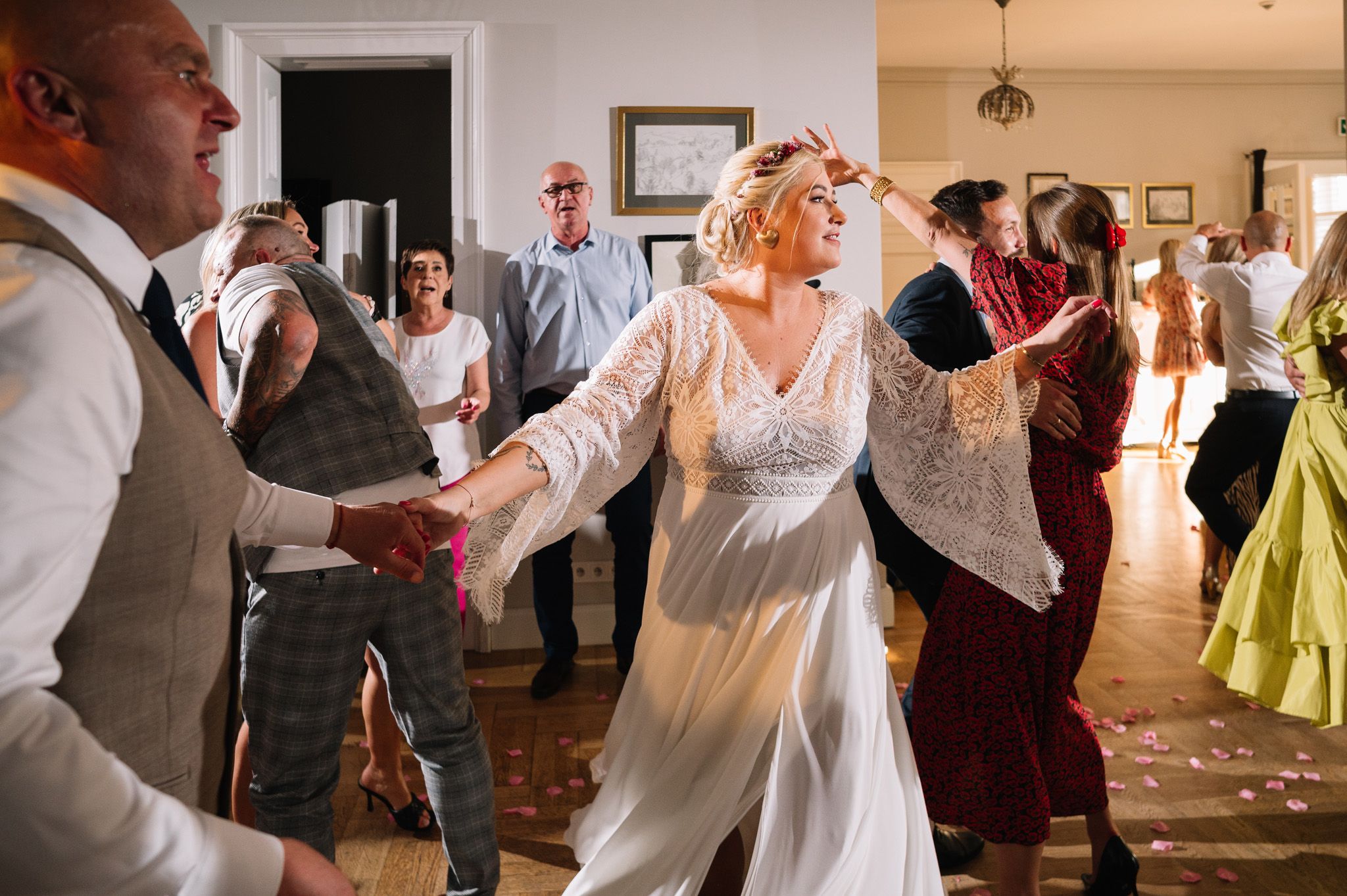 Wedding celebration with guests dancing joyfully in a light-filled room with wooden floors.