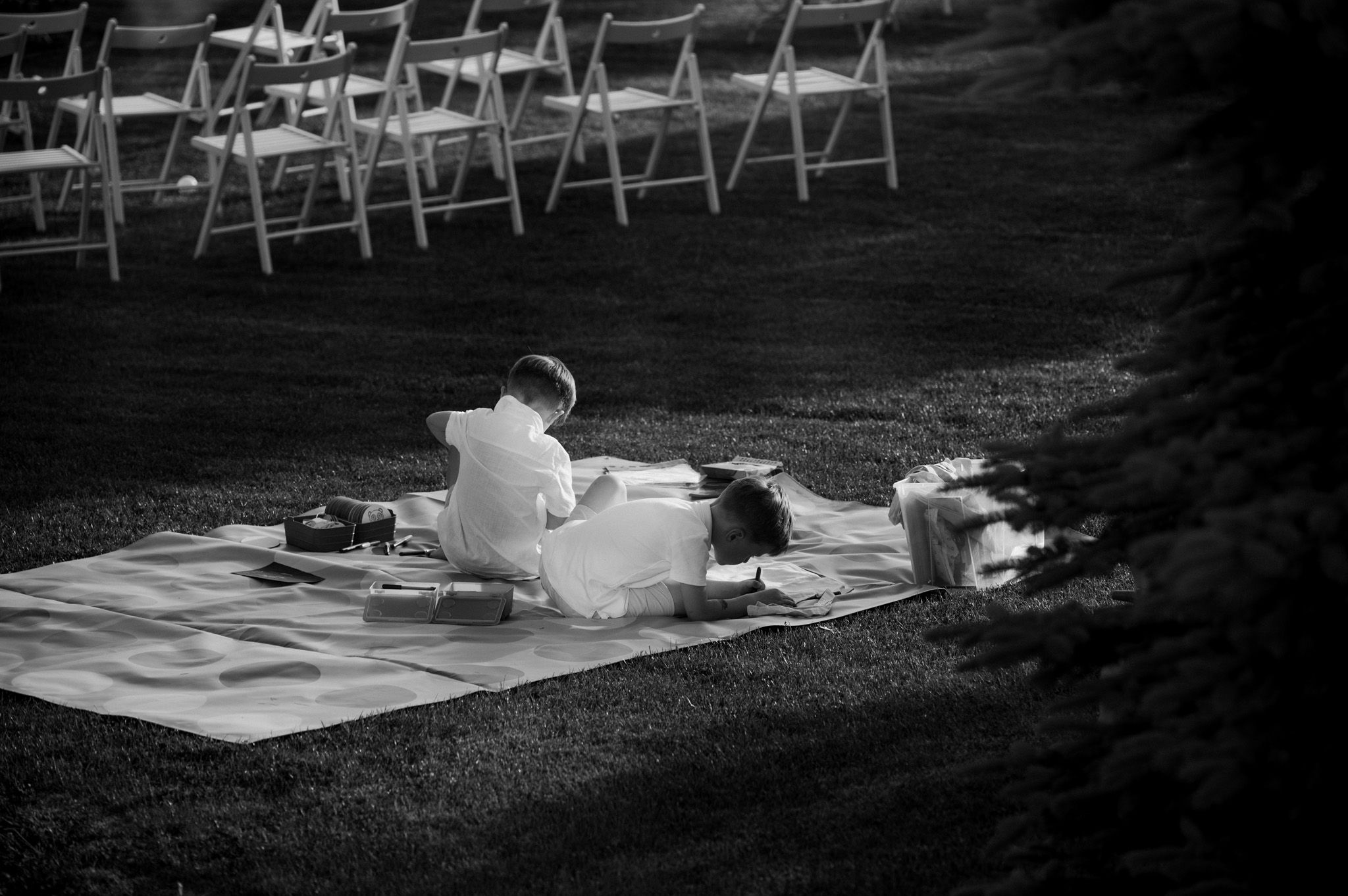 Black and white photo of person sitting on blanket near row of outdoor ceremony chairs.