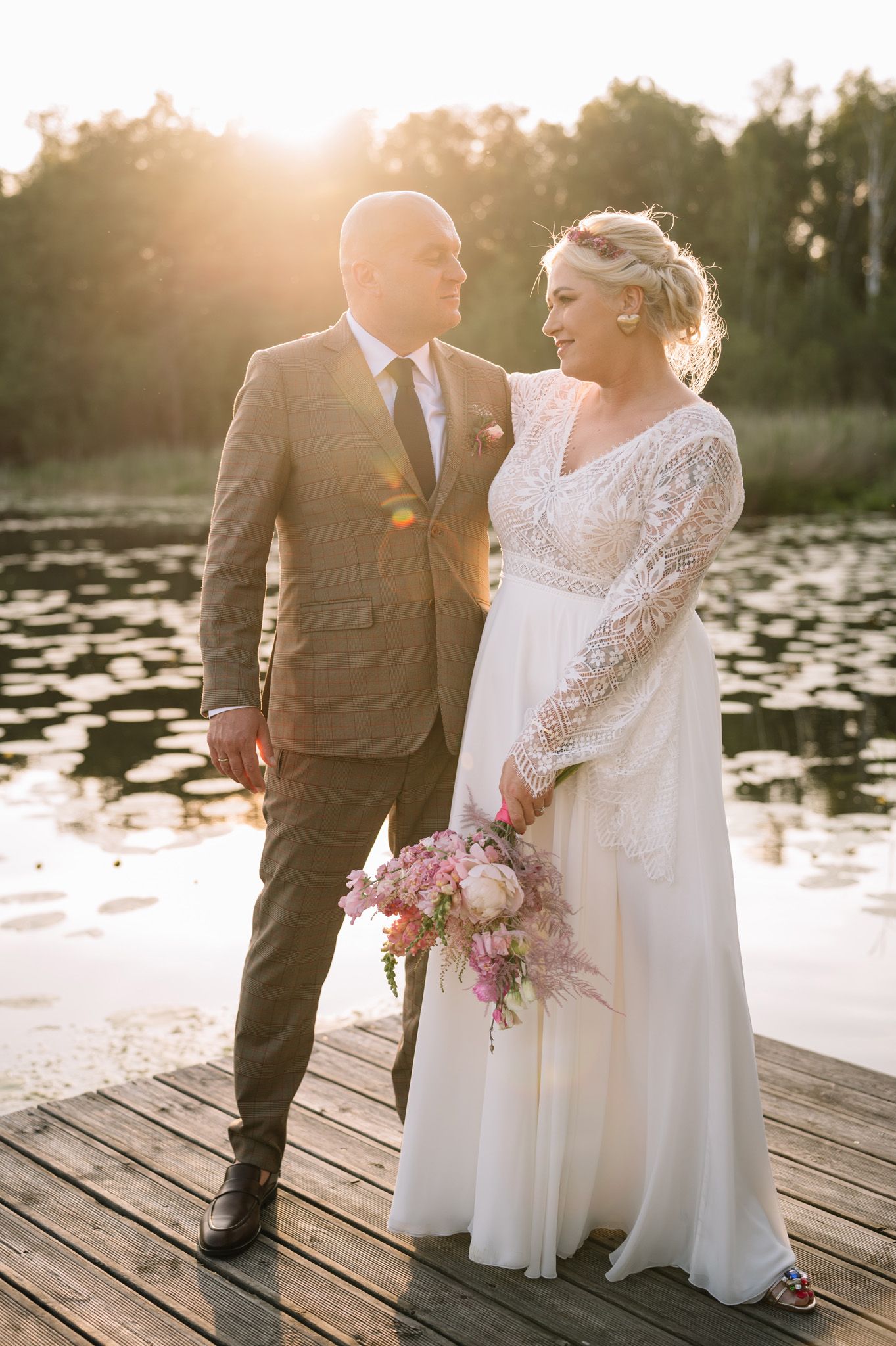 Sunset wedding portrait of couple standing on dock with lily pond in background.