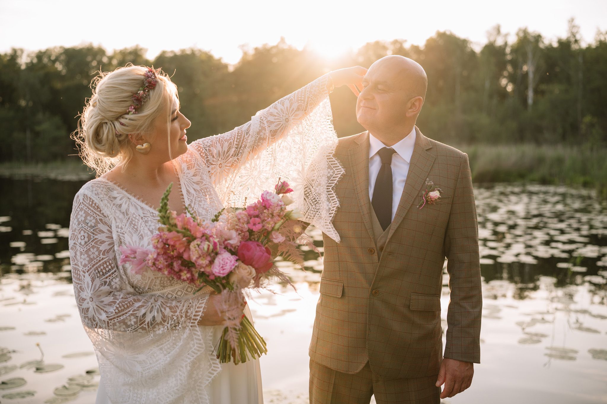 Romantic wedding couple embracing in sunset light by a lake with lily pads.