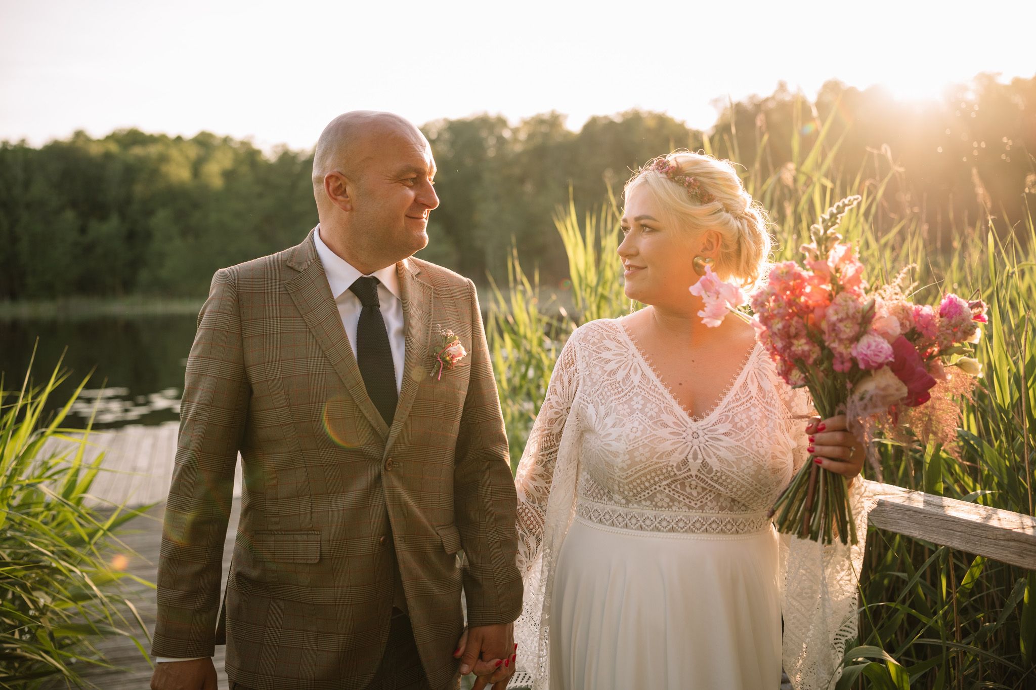 Newlyweds walking together along lakeside in warm evening sunlight.