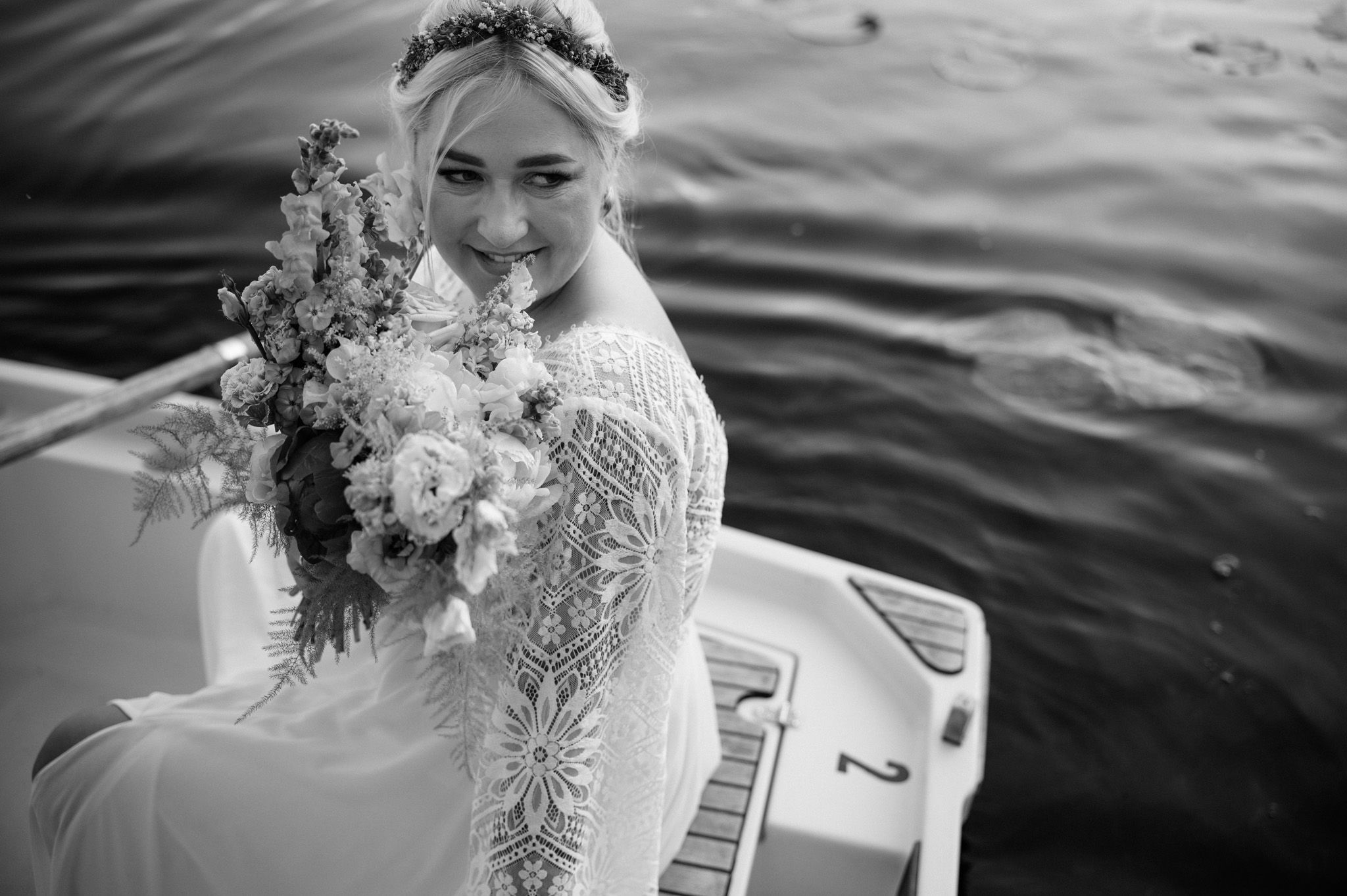 Black and white photo of bride with bouquet sitting in boat on water.