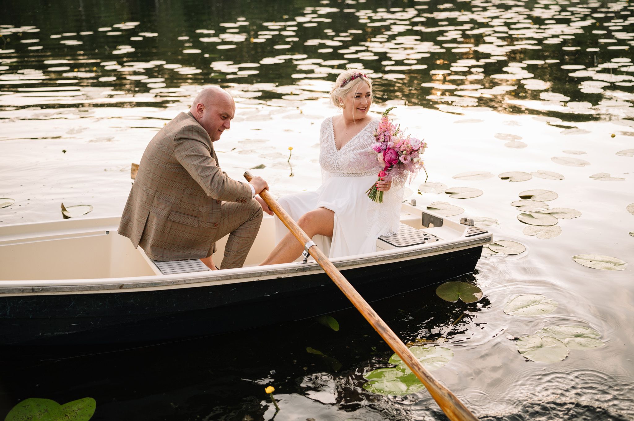 Couple sitting together in wooden rowboat on lake with lily pads.
