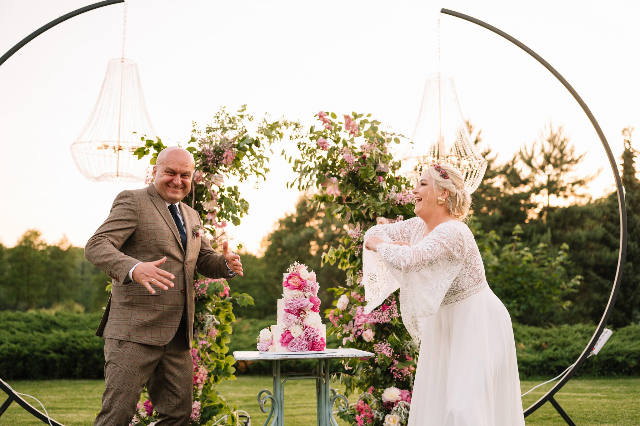 A couple celebrates near a decorated cake table in an outdoor garden setting.