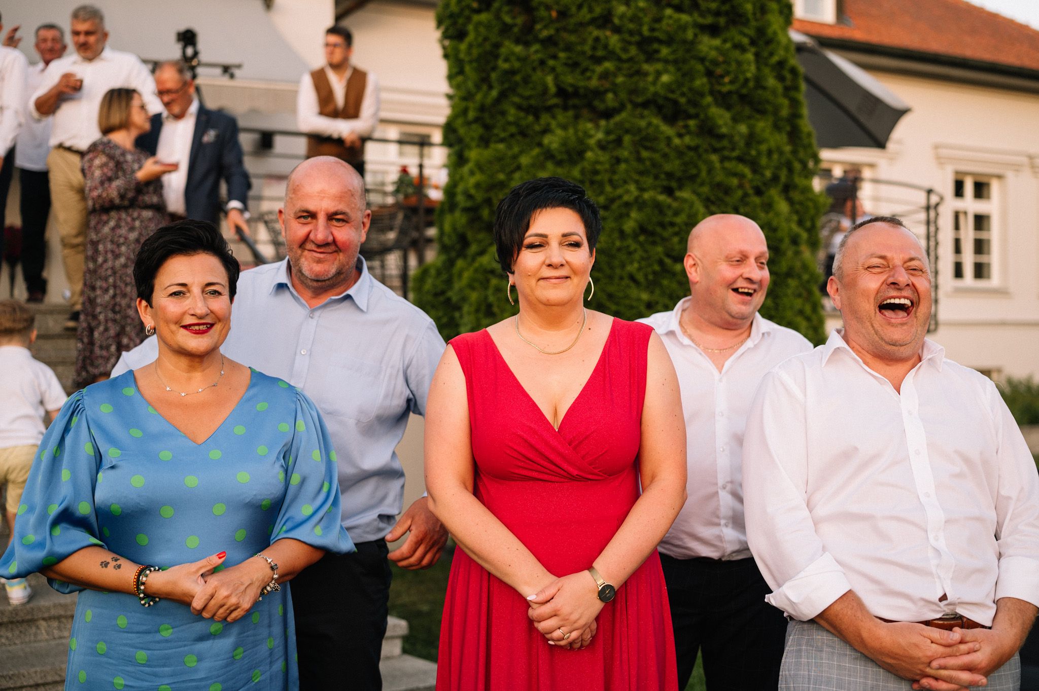 Wedding guests in formal attire seated outdoors and smiling during celebration.