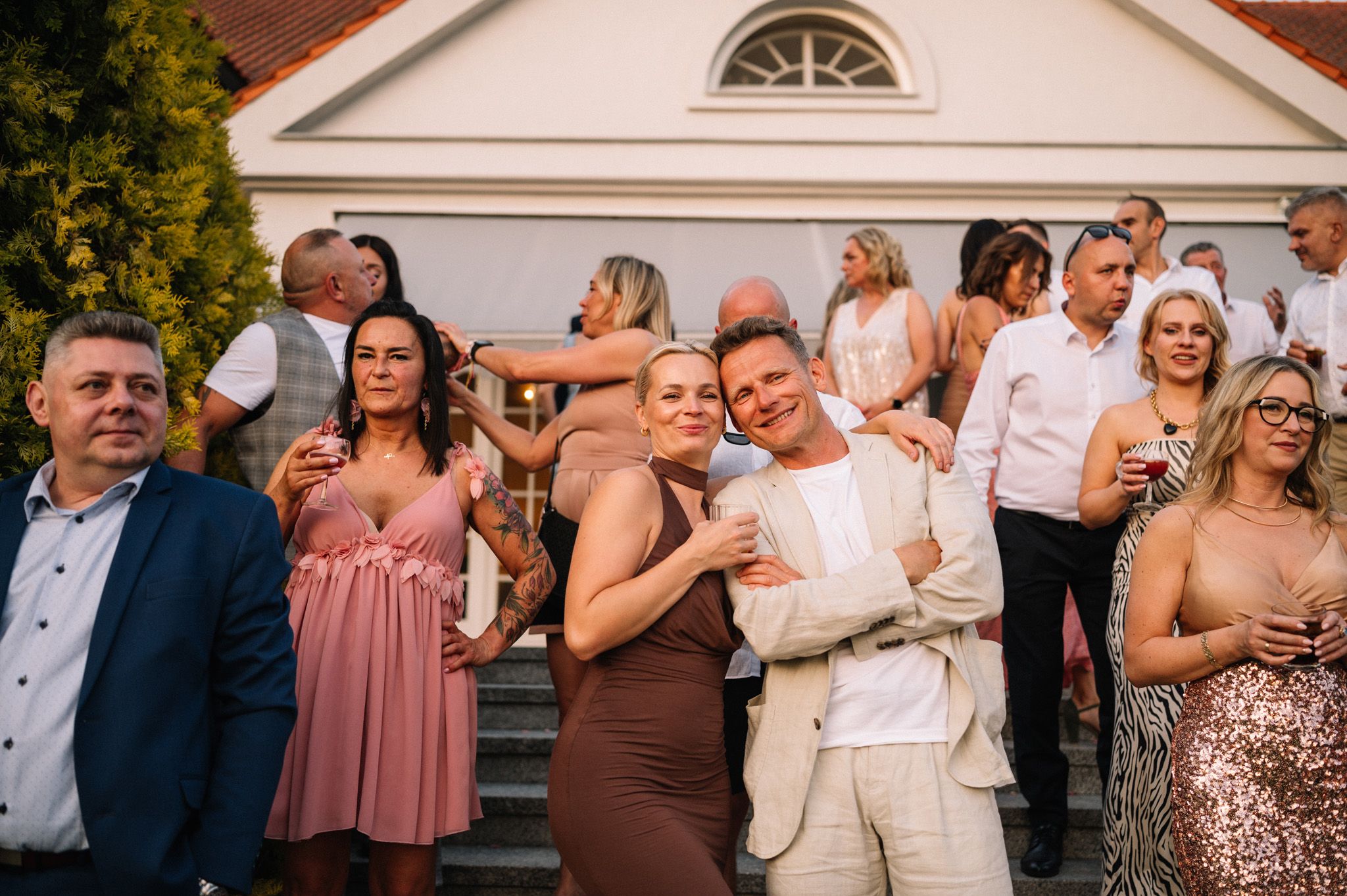 Group of wedding guests gathered on steps in colorful attire during outdoor celebration.