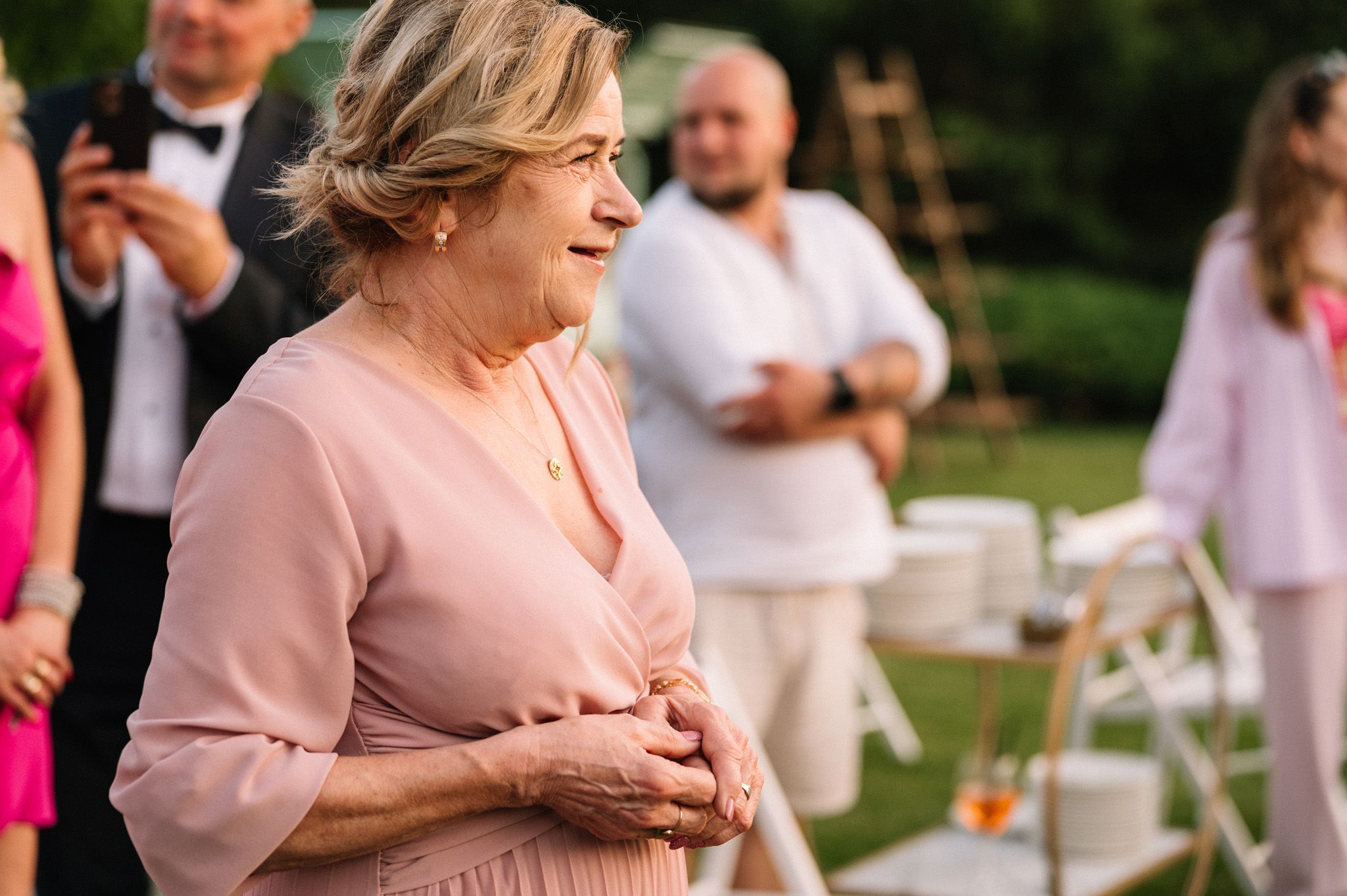 Person in pink dress laughing joyfully during outdoor garden party.