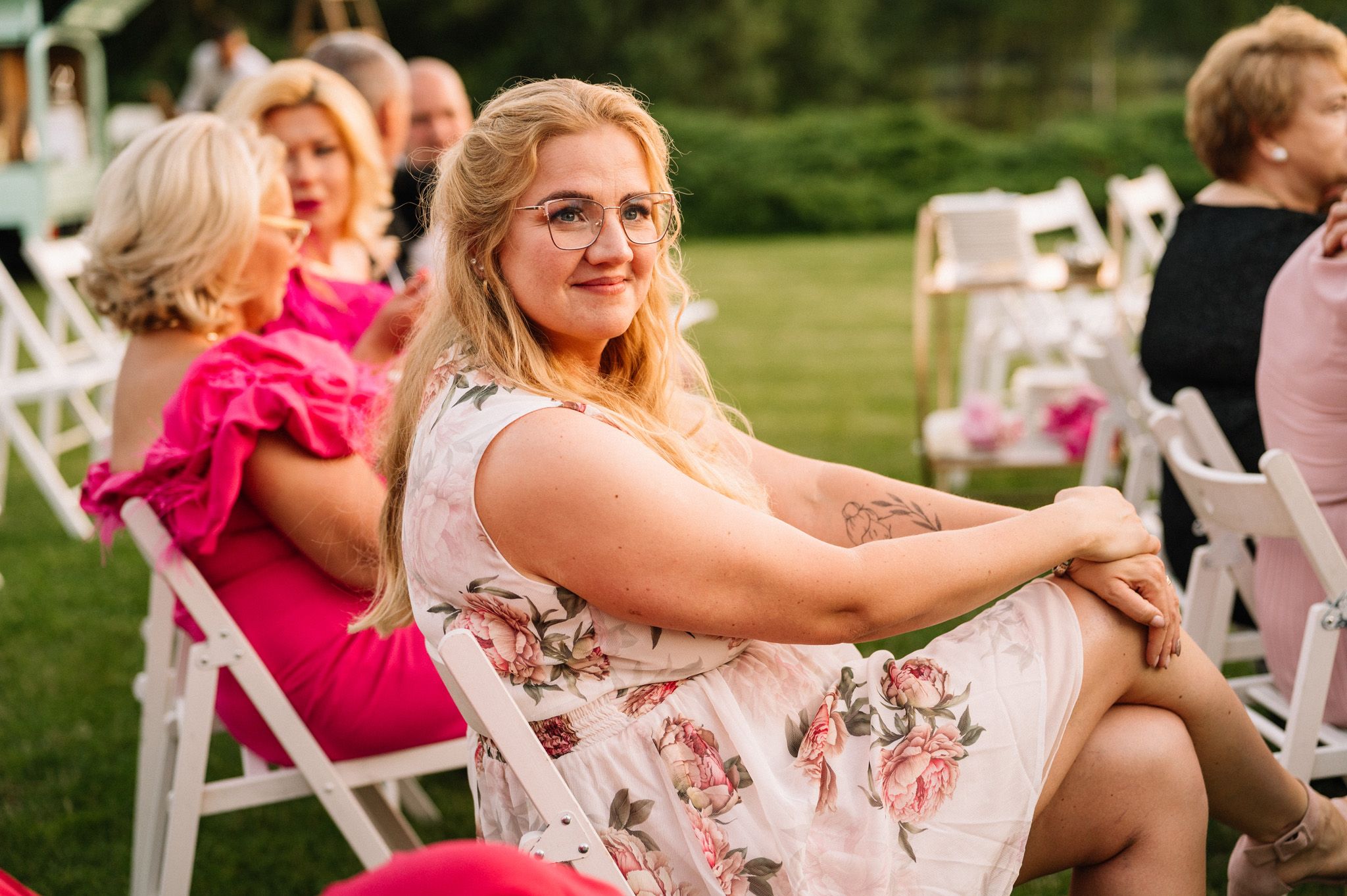 Guest in floral dress sitting on white folding chair at outdoor celebration.