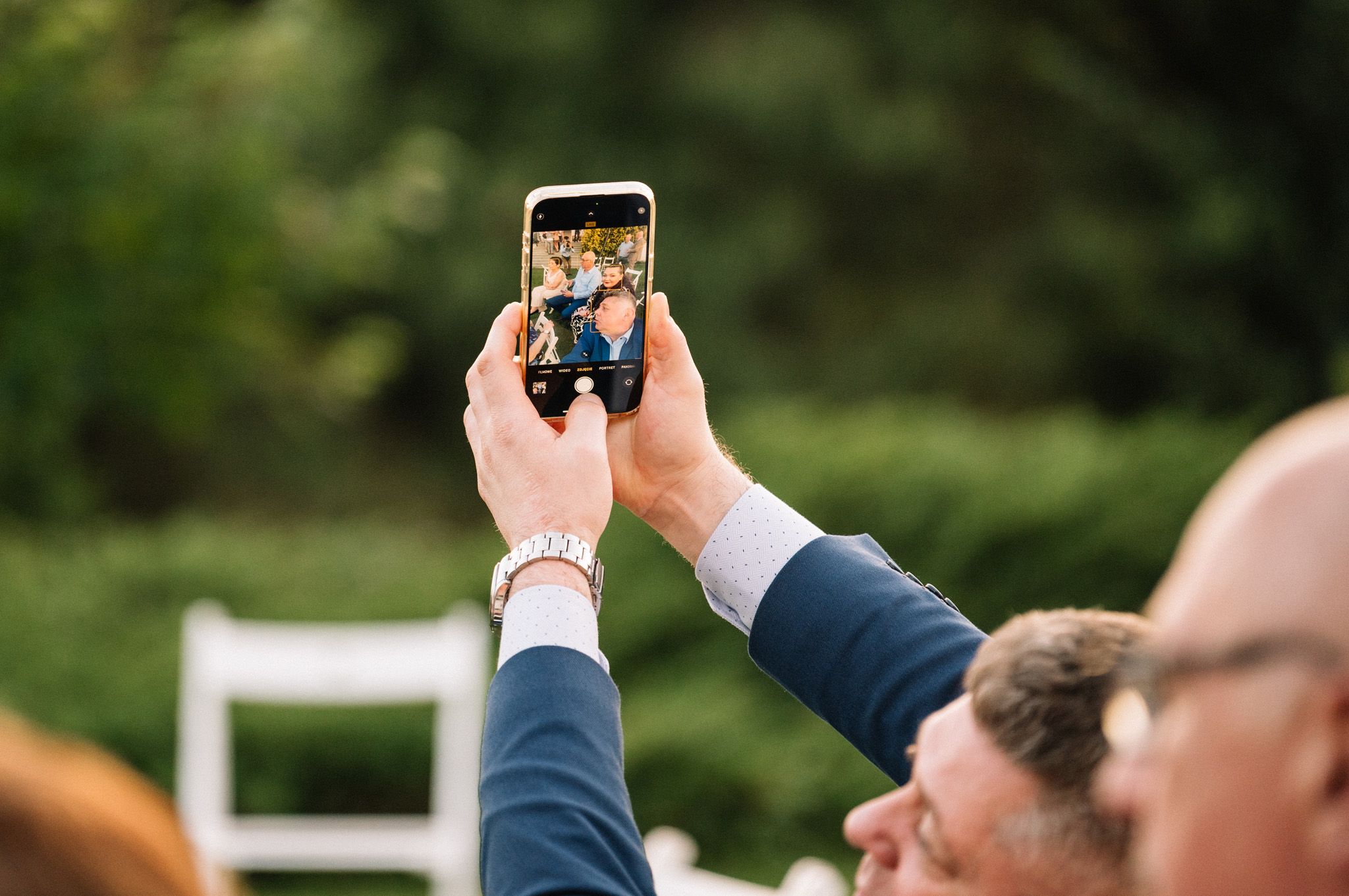 Hand holding smartphone to capture photos during outdoor wedding celebration.