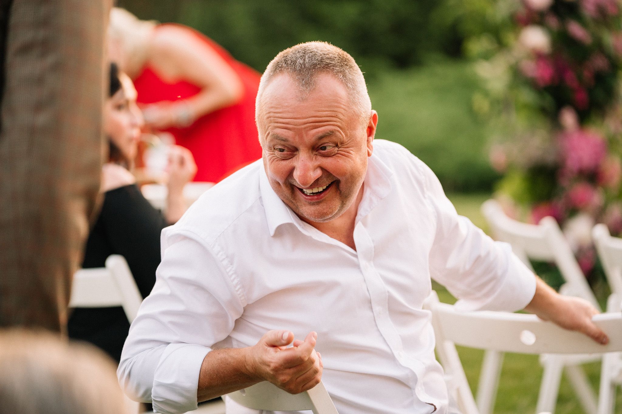 Guest in white shirt laughing heartily during outdoor celebration.
