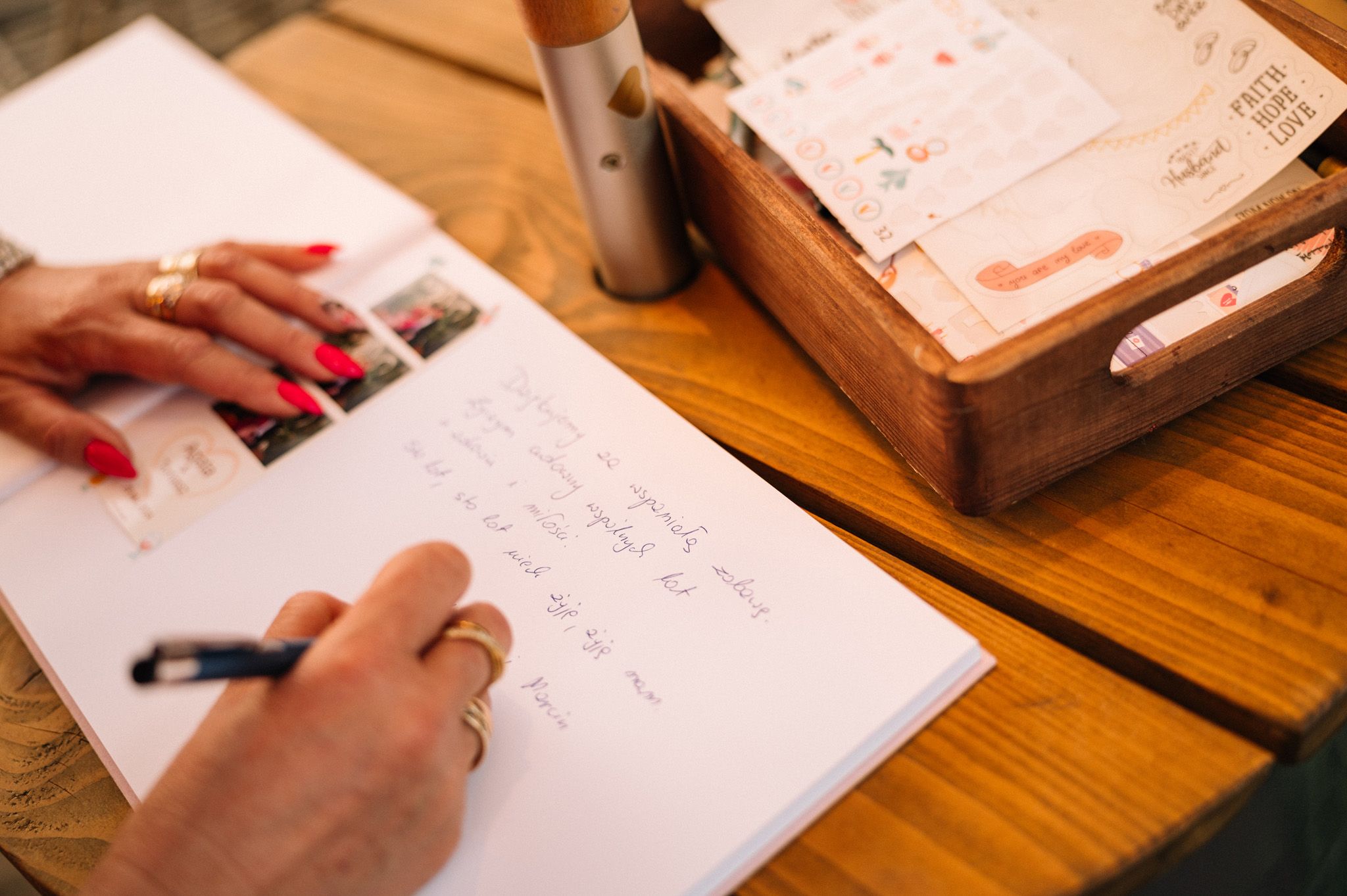 Hands writing in guest book on wooden table with decorative box nearby.