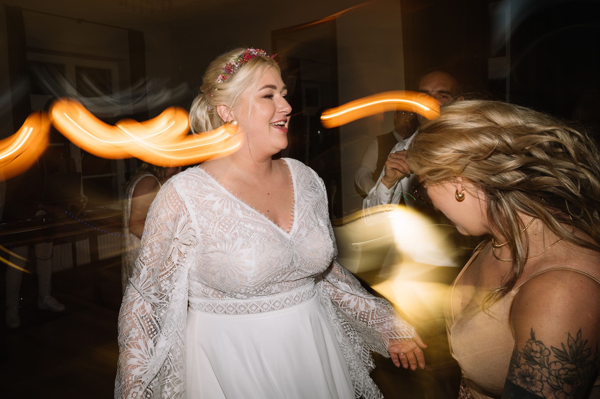 Wedding guests dance energetically on the dance floor with motion blur and glowing light trails in the background.