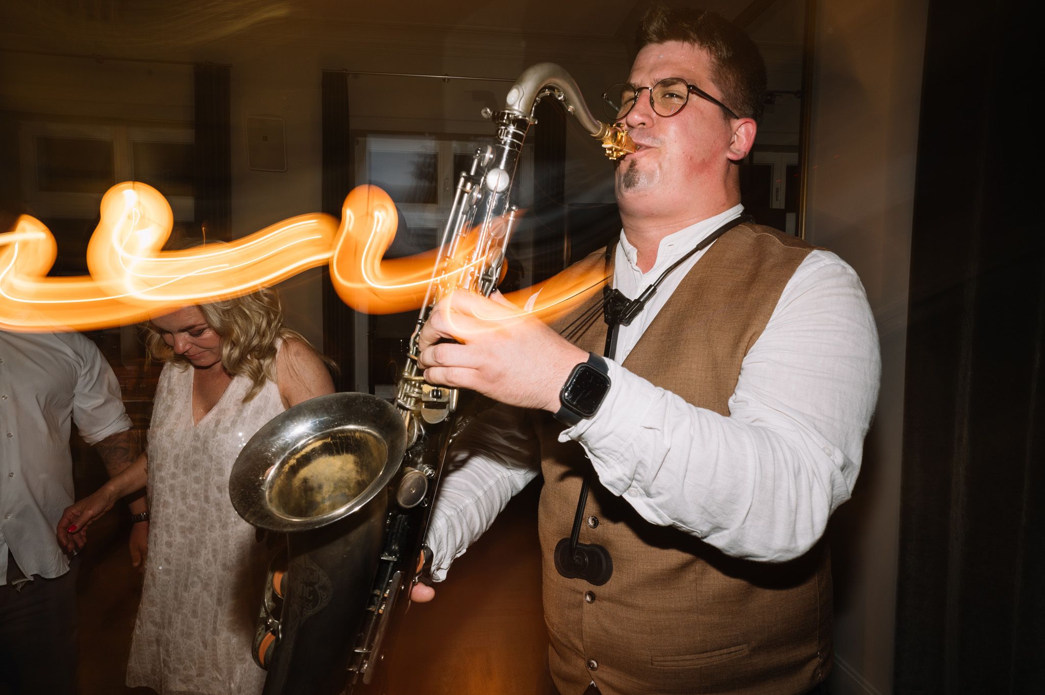 Musician plays saxophone at wedding reception with motion blur effects in background.