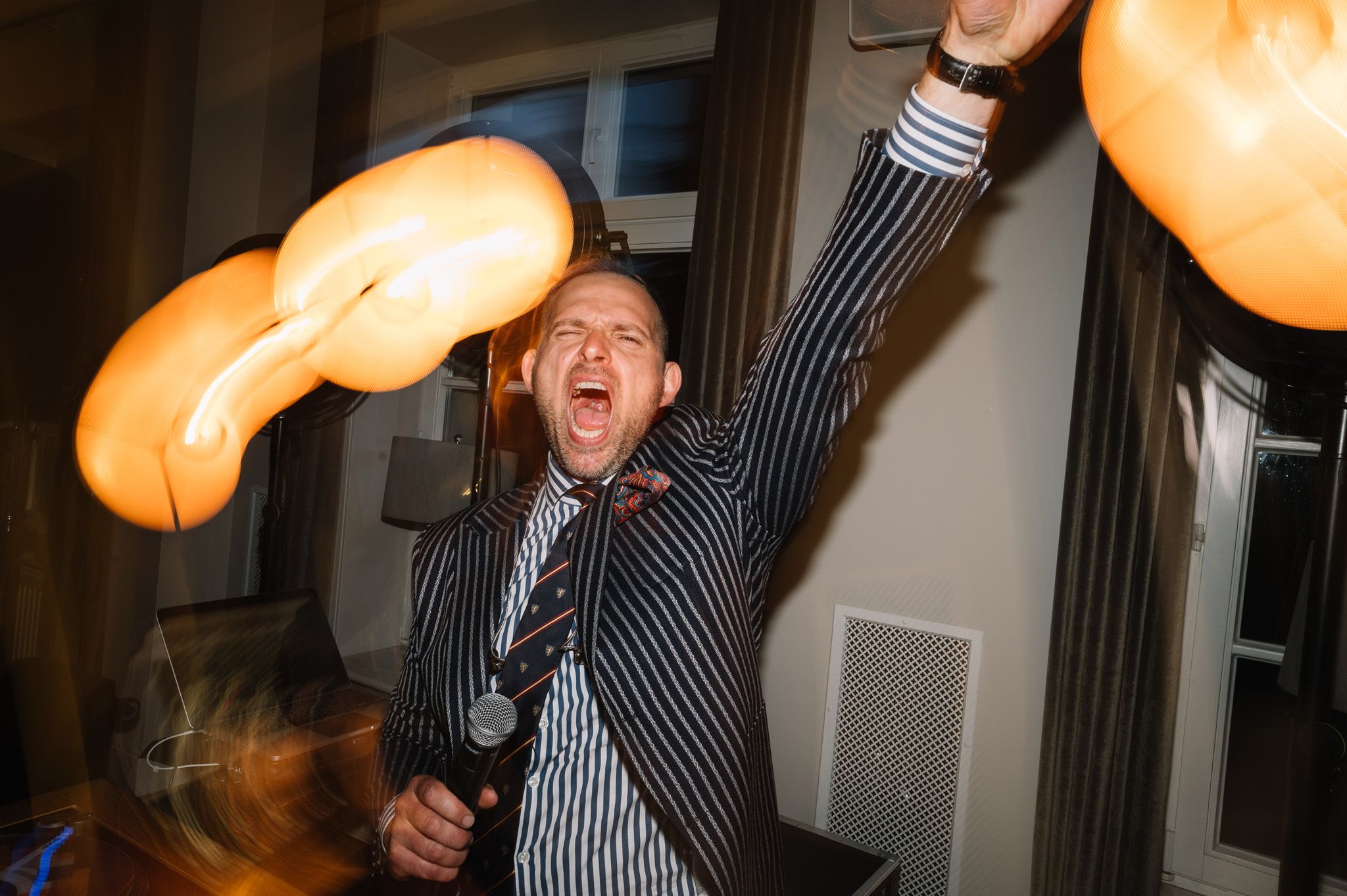 Party guest in striped jacket dances enthusiastically with light trails creating dynamic motion effect.